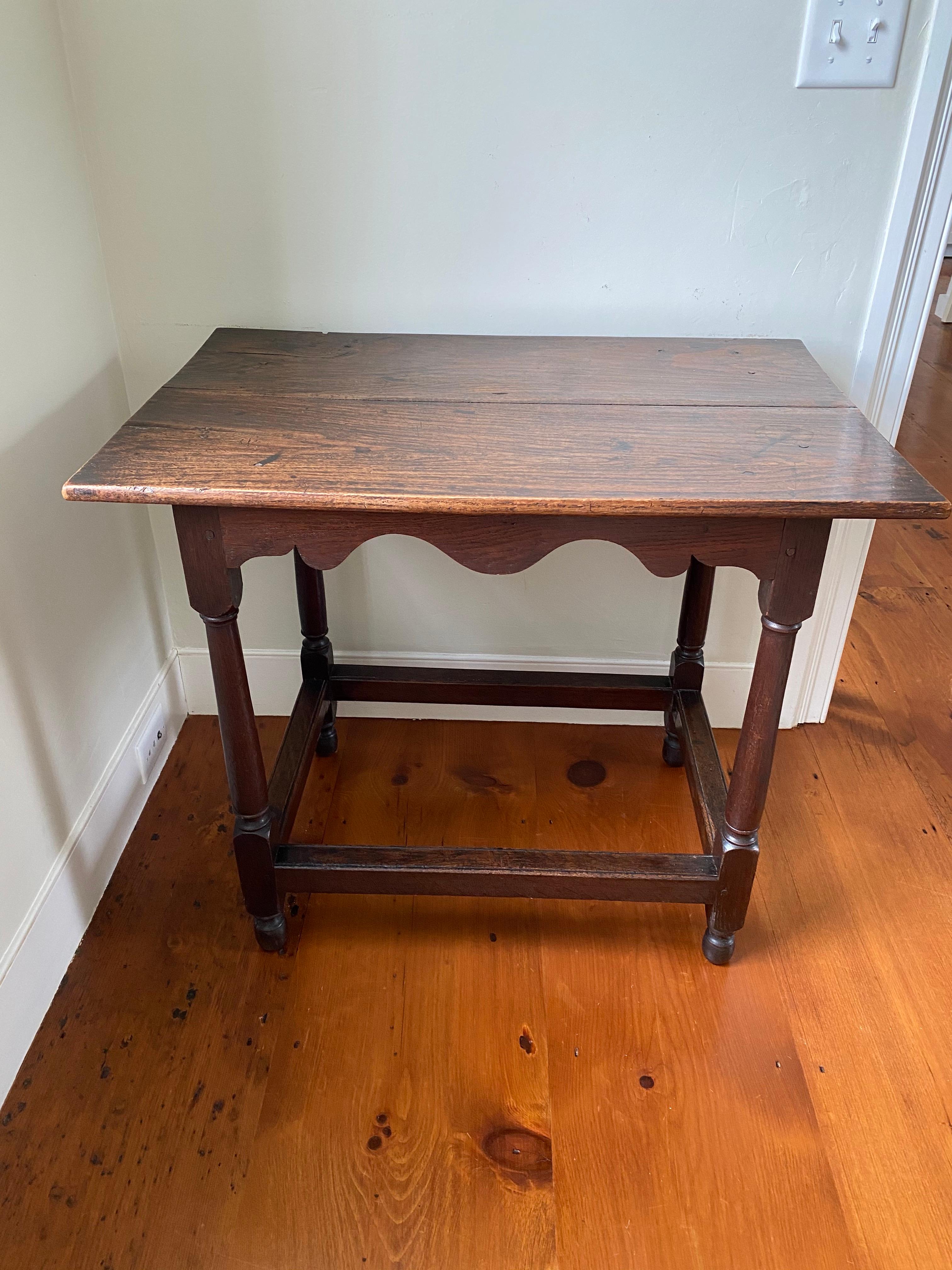19th Century English oak tavern table with two board top, boldly shaped scalloped apron, turned legs and blocked stretcher base.
