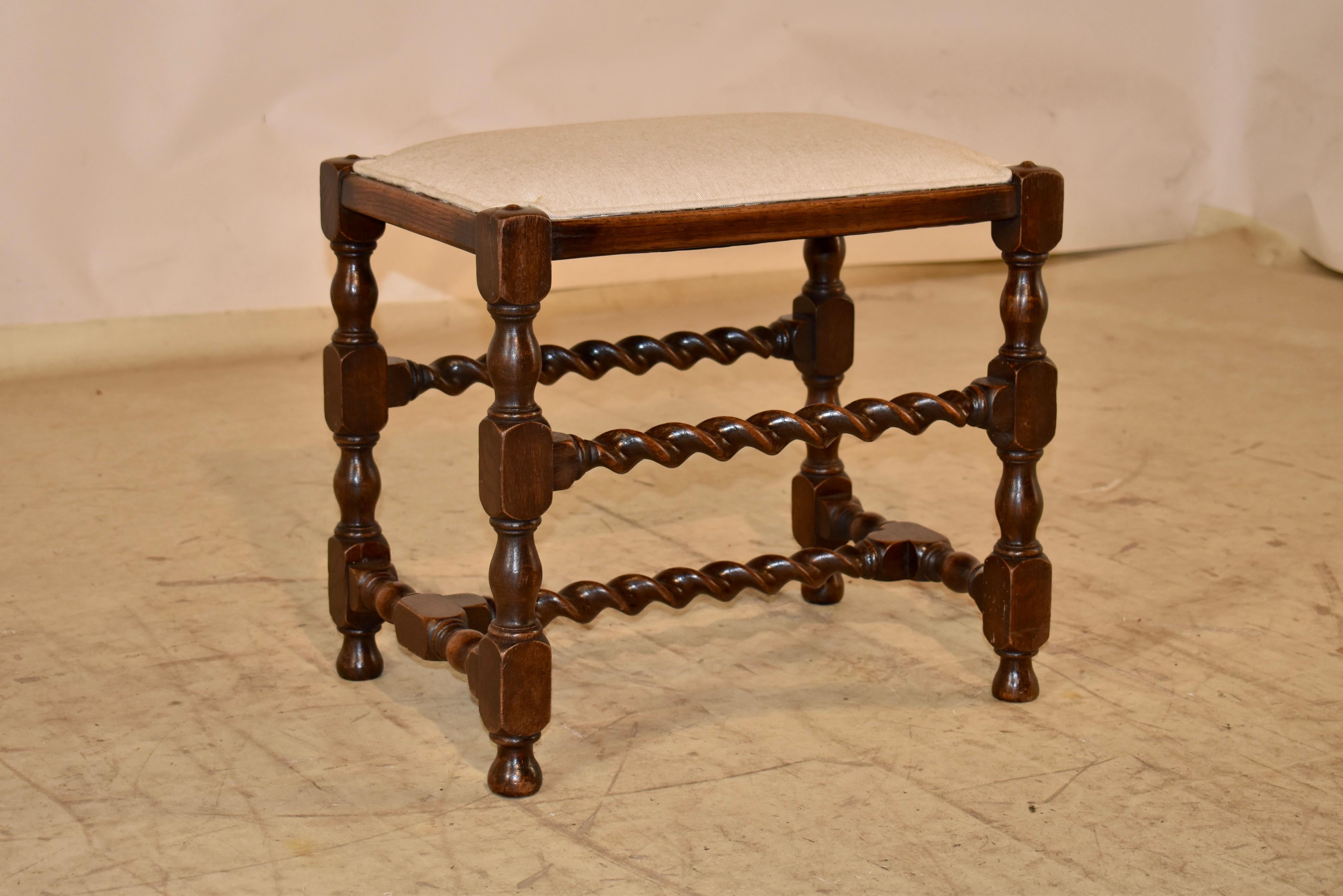 Taburete torneado de roble del siglo XIX, procedente de Inglaterra, con el asiento recién tapizado en lino.  La encimera de lino tiene un ribete decorativo sencillo que rodea el asiento y acentúa los botones torneados de la parte superior de las