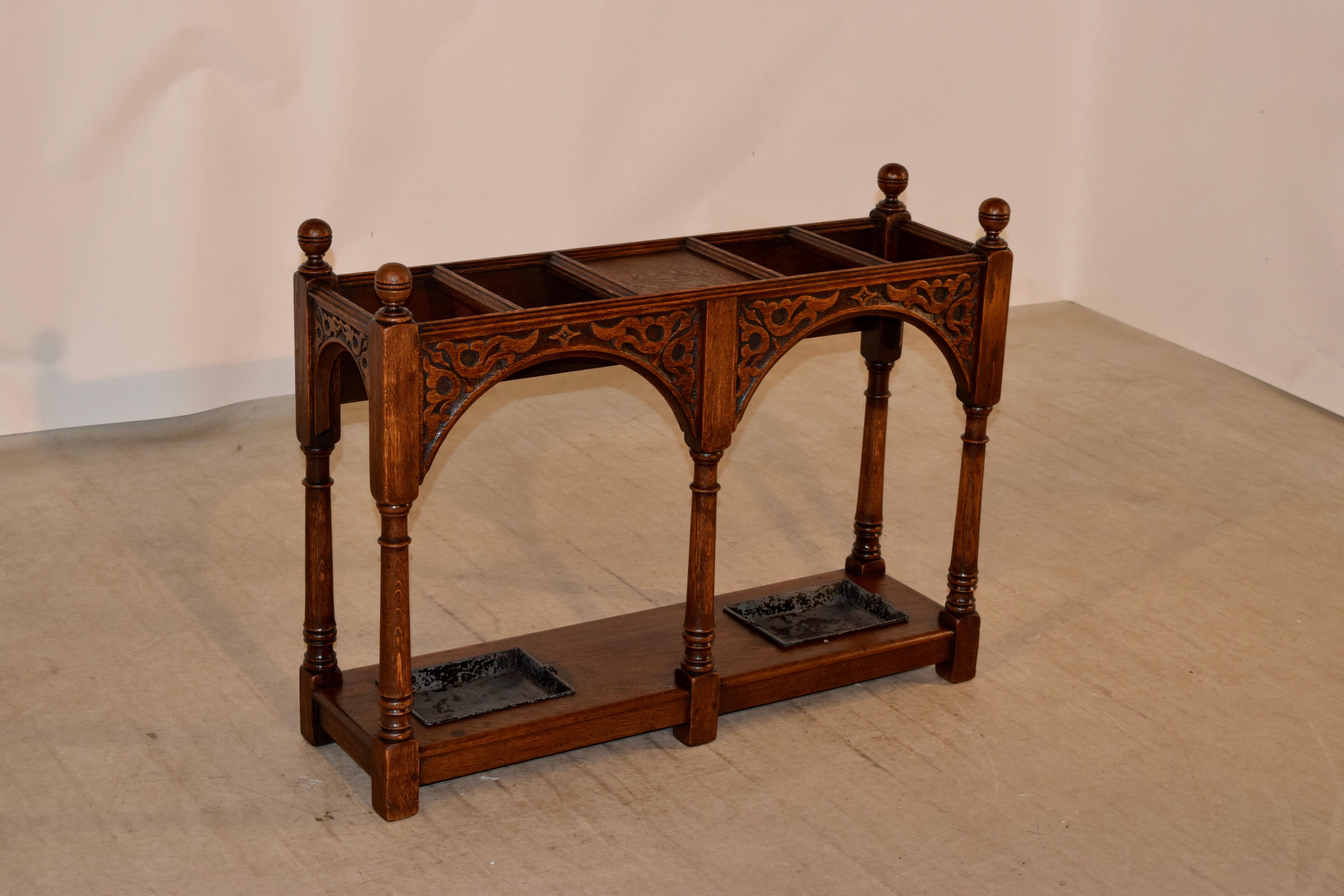 19th century English oak umbrella stand with four sections for umbrellas or canes and two drip trays below. The top has hand-turned finials over a molded edge and shaped aprons with hand carved decoration on three sides. The back side is plain for