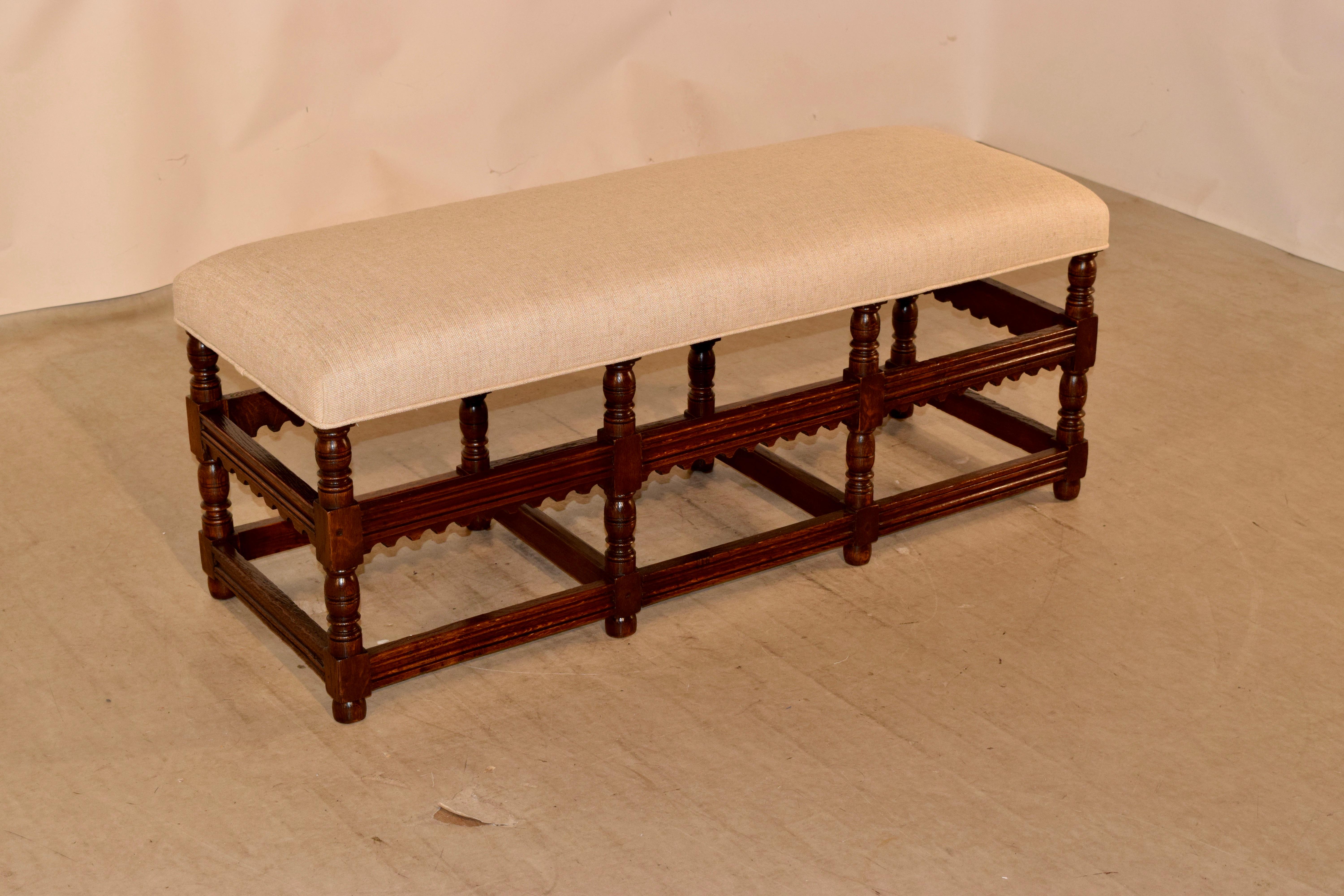 19th century English oak bench with newly upholstered seat in linen finished with a single welt. The frame is made from English oak and has lovely hand turned legs joined by hearty stretchers with routed decoration and the top stretcher shaped in