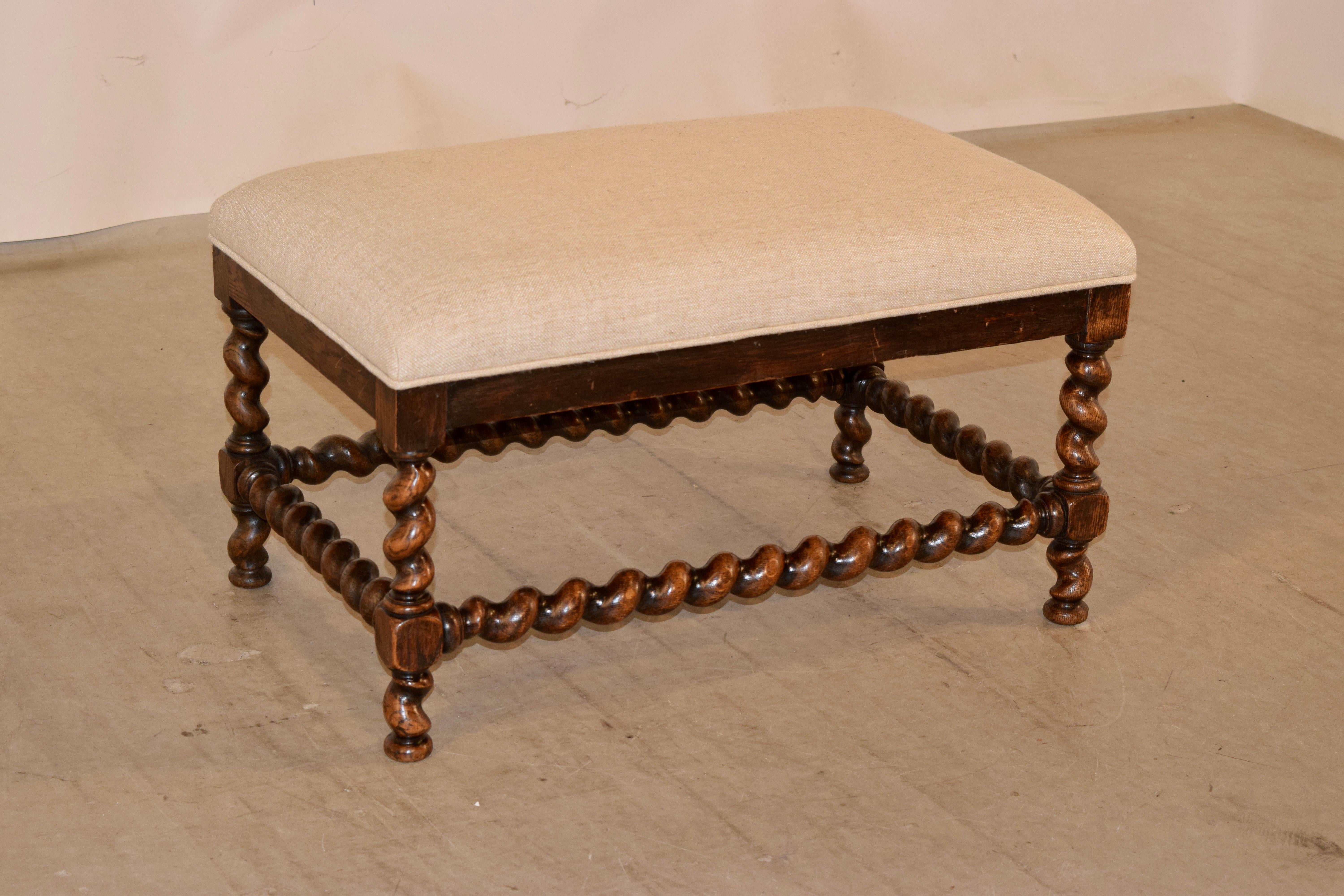 19th century oak bench from England with a newly upholstered seat in linen, finished with a single welt decoration, following down to exquisitely hand turned legs and matching stretchers. The feet are also hand turned barley twist, which is very