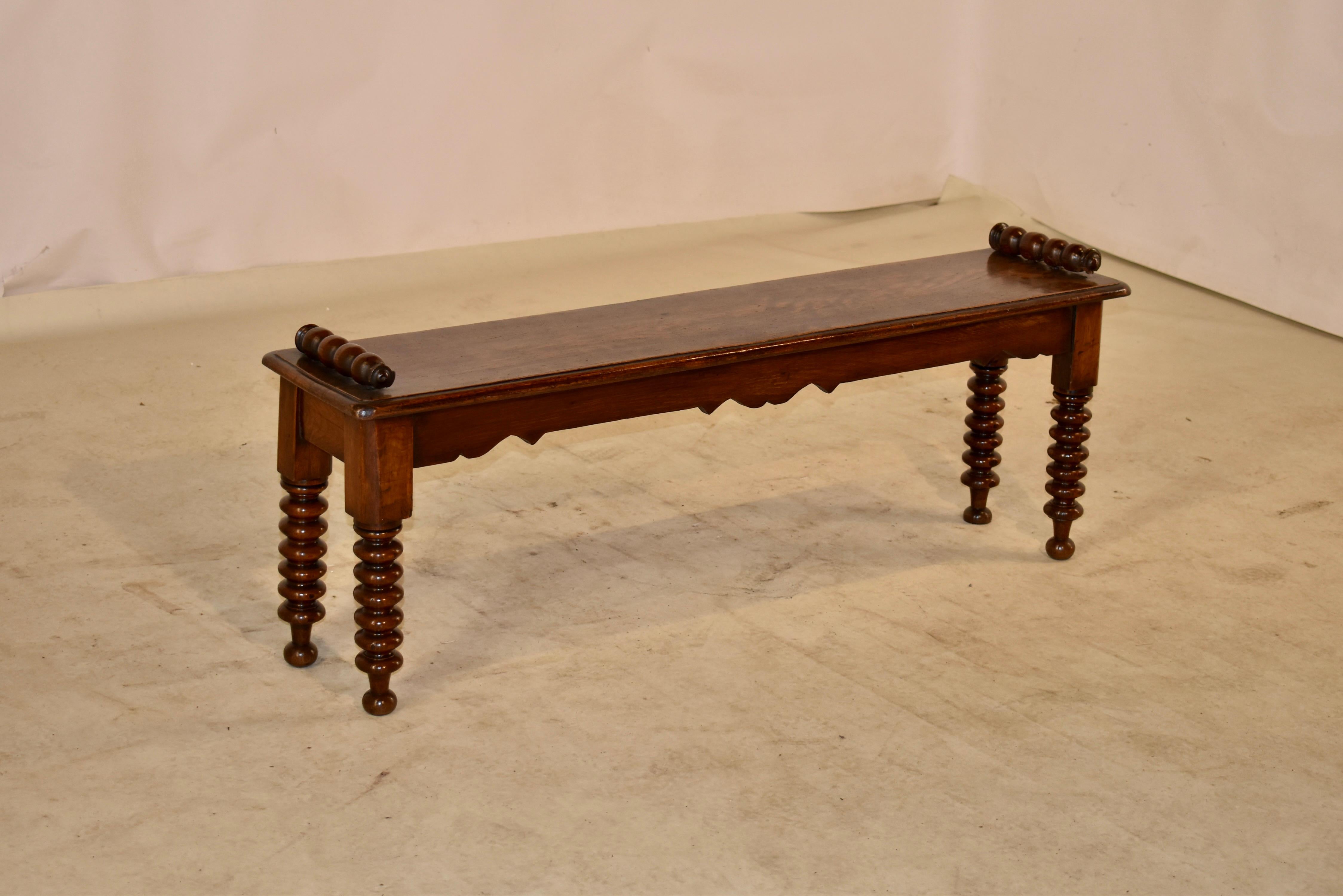 19th century oak window seat from England with hand turned applied handle on the top of the seat, which has a beveled edge and follows down to a scalloped apron. The bench is supported on hand turned bobbin type legs and raised on hand turned feet.