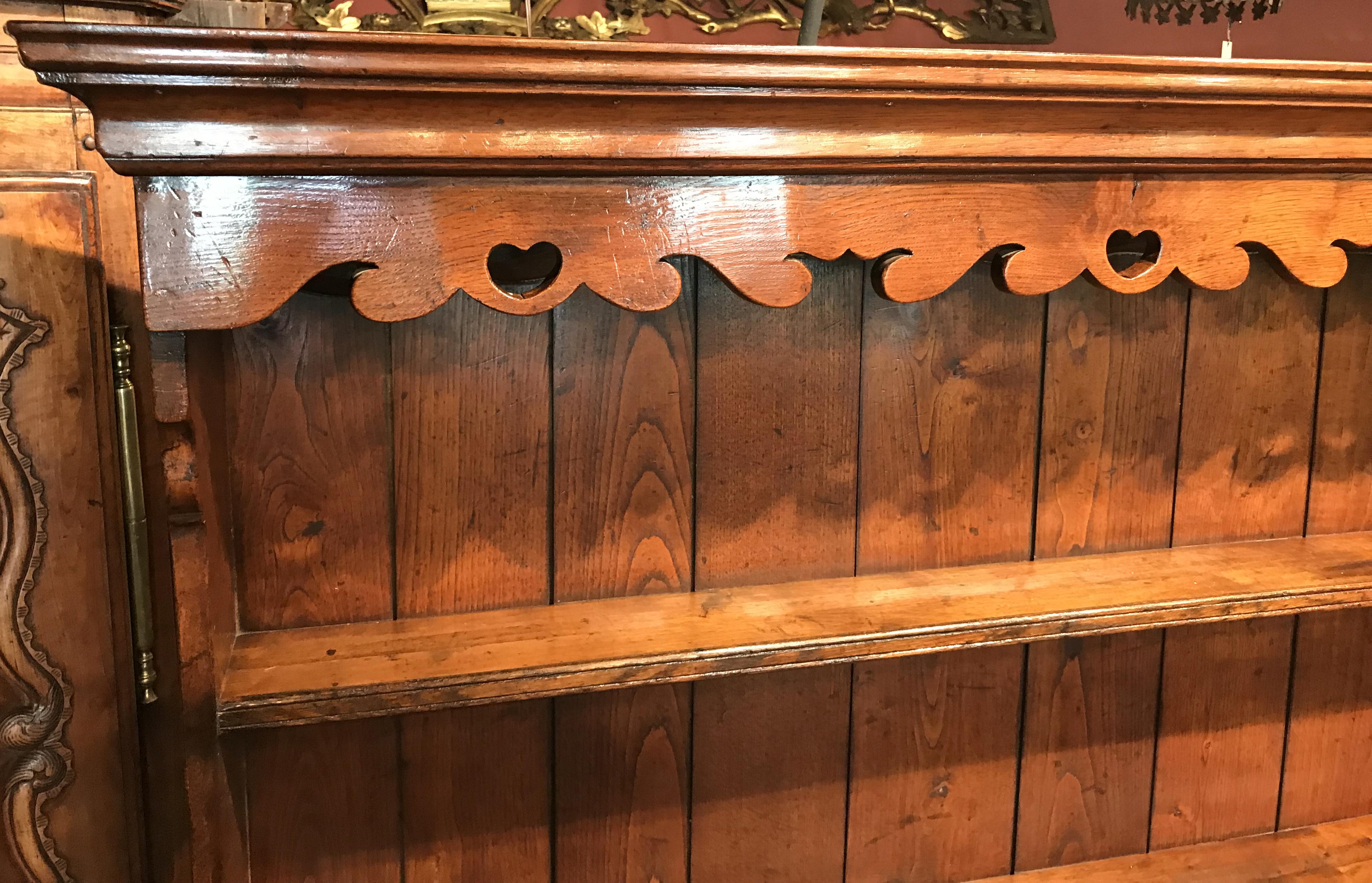 A fine English or Welsh two-part dresser, its upper section with a molded cornice surmounting a nice scroll-carved crown with heart cutouts over two open shelves with plate rails and tongue and grooved backboards, over a row of fitted spice drawers,
