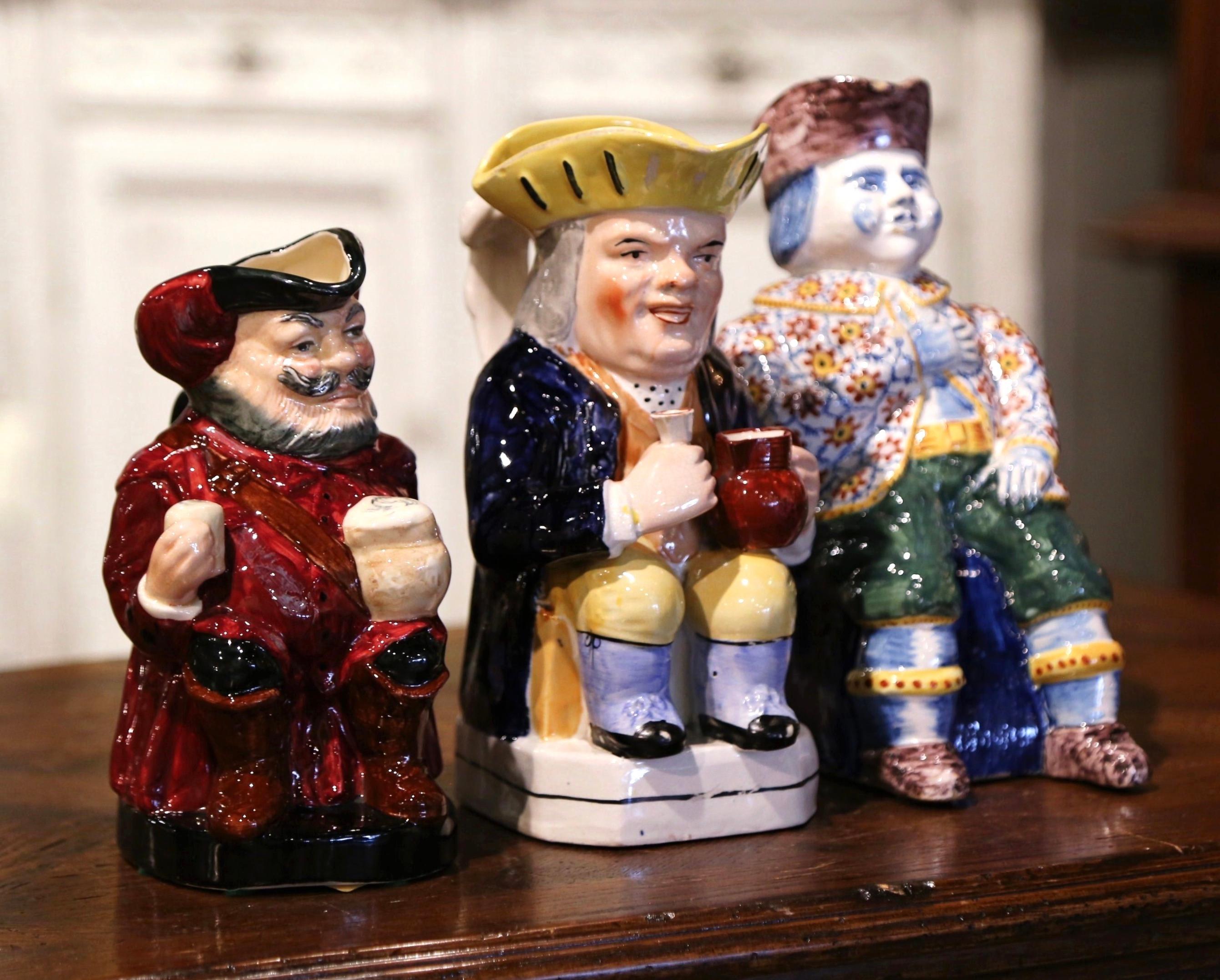 Decorate a wet bar with this charming, sculptural set of antique majolica pitchers. Crafted in England circa 1890, each colorful barbotine jug similar to the one of Onnaing, features three guys in a sitting position and drinking. The body and handle