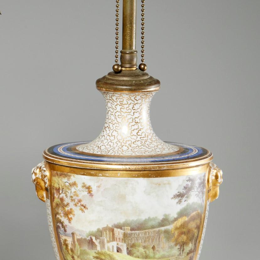 19th c. English urn converted to a table lamp with vermiculated gilt and polychrome enamel on porcelain, a stone base and a brass stem and socket. One side depicts a lovely English pastoral scene with a large stone building in the background. The
