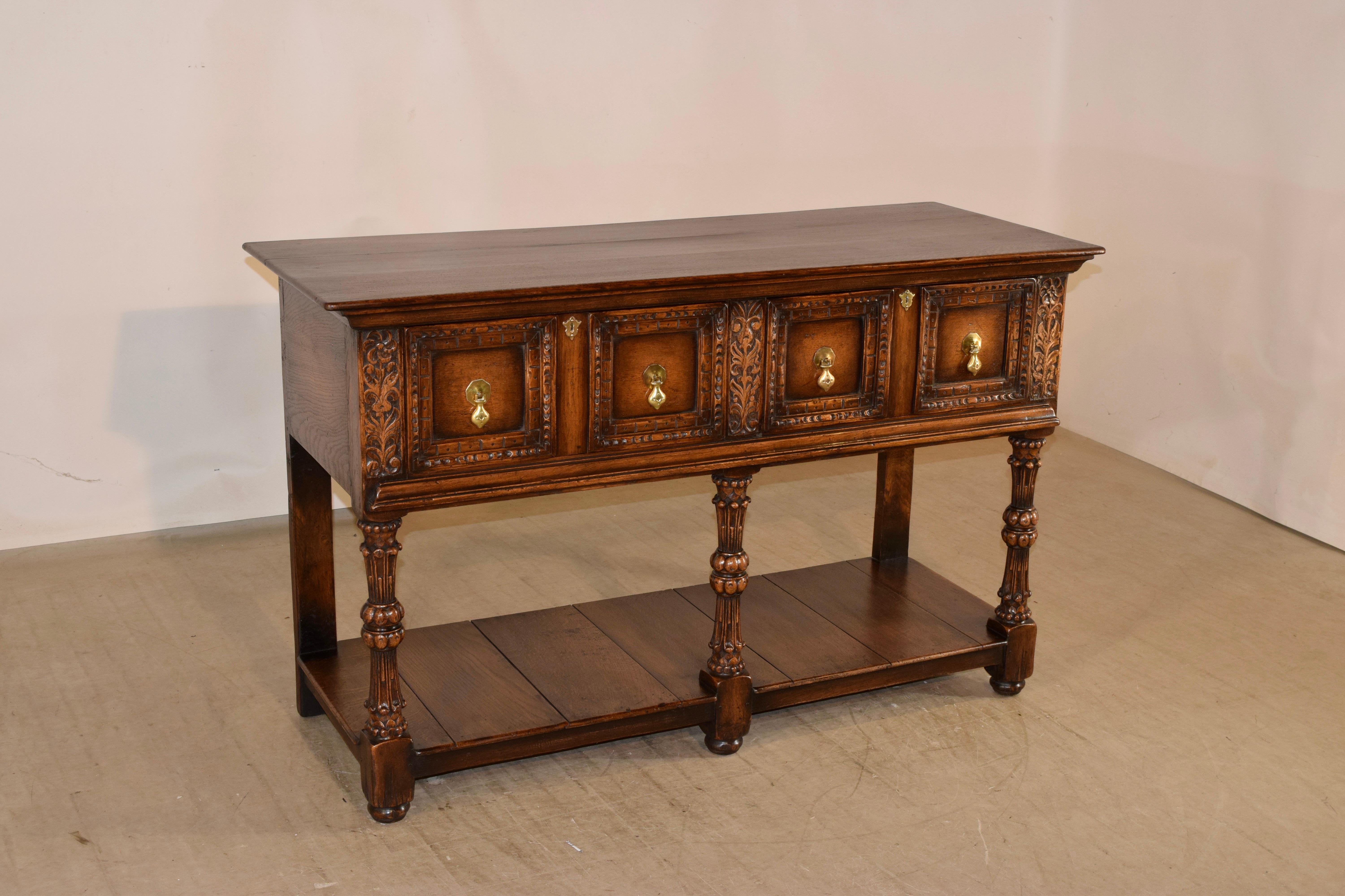 19th Century English oak sideboard with a plank top following down to simple sides and two paneled and carved drawers in the front, flanked by floral carved panels over a molded edge. The piece is supported on three wonderfully carved and