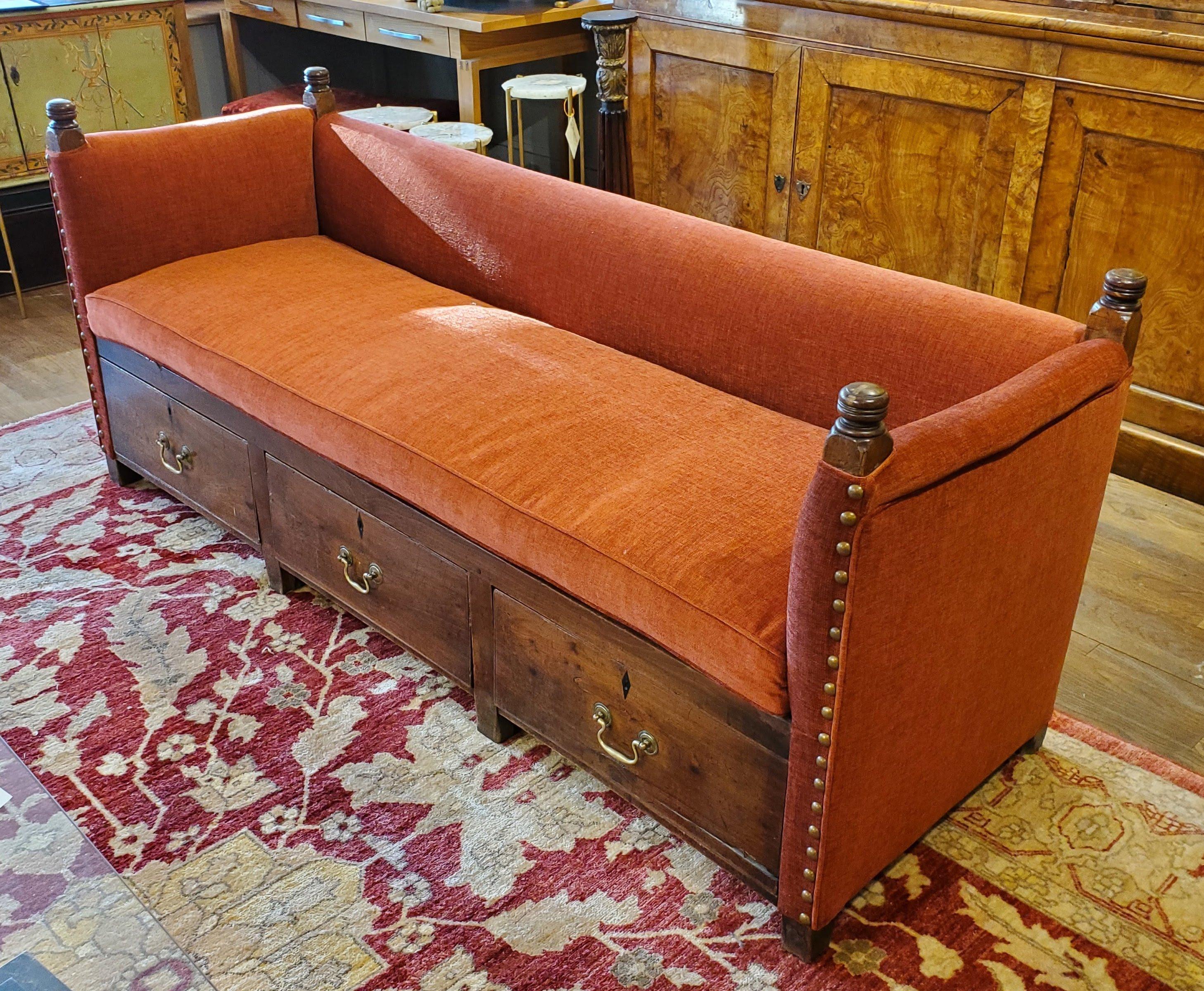 This unusual 19th century English upholstered bench is a stunner. Made of richly patinated oak with three drawers, four turned posts and original brass hardware. Recently reupholstered in a soft persimmon fabric with large brass nailhead decoration.