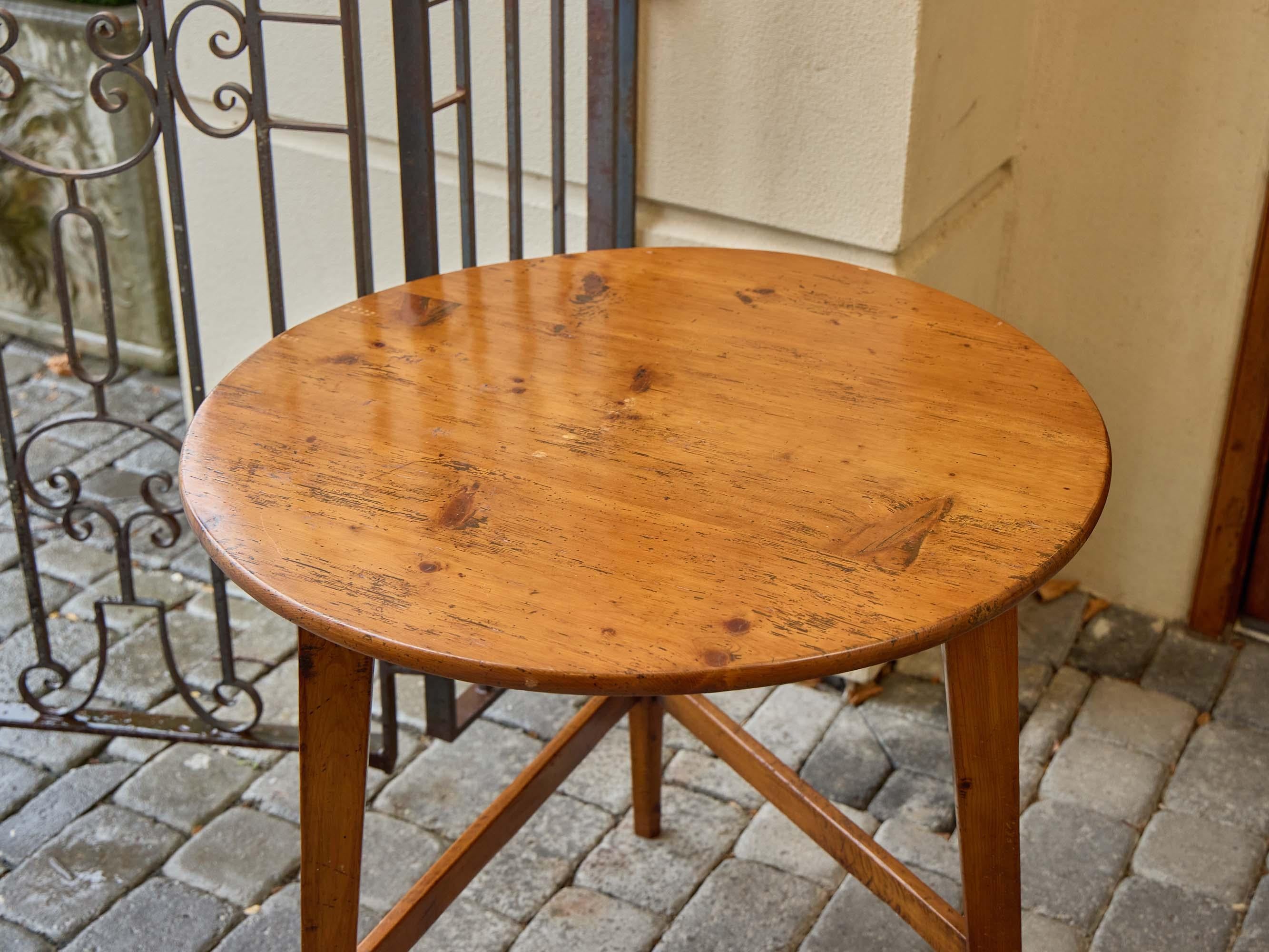 Dieser Cricket-Tisch aus dem 19. Jahrhundert ist ein klassisches Beispiel für englische Landhausmöbel. Er ist aus warm patiniertem Kiefernholz gefertigt und zeichnet sich durch eine ruhige, zweckmäßige Eleganz aus. Die runde Platte ruht auf drei