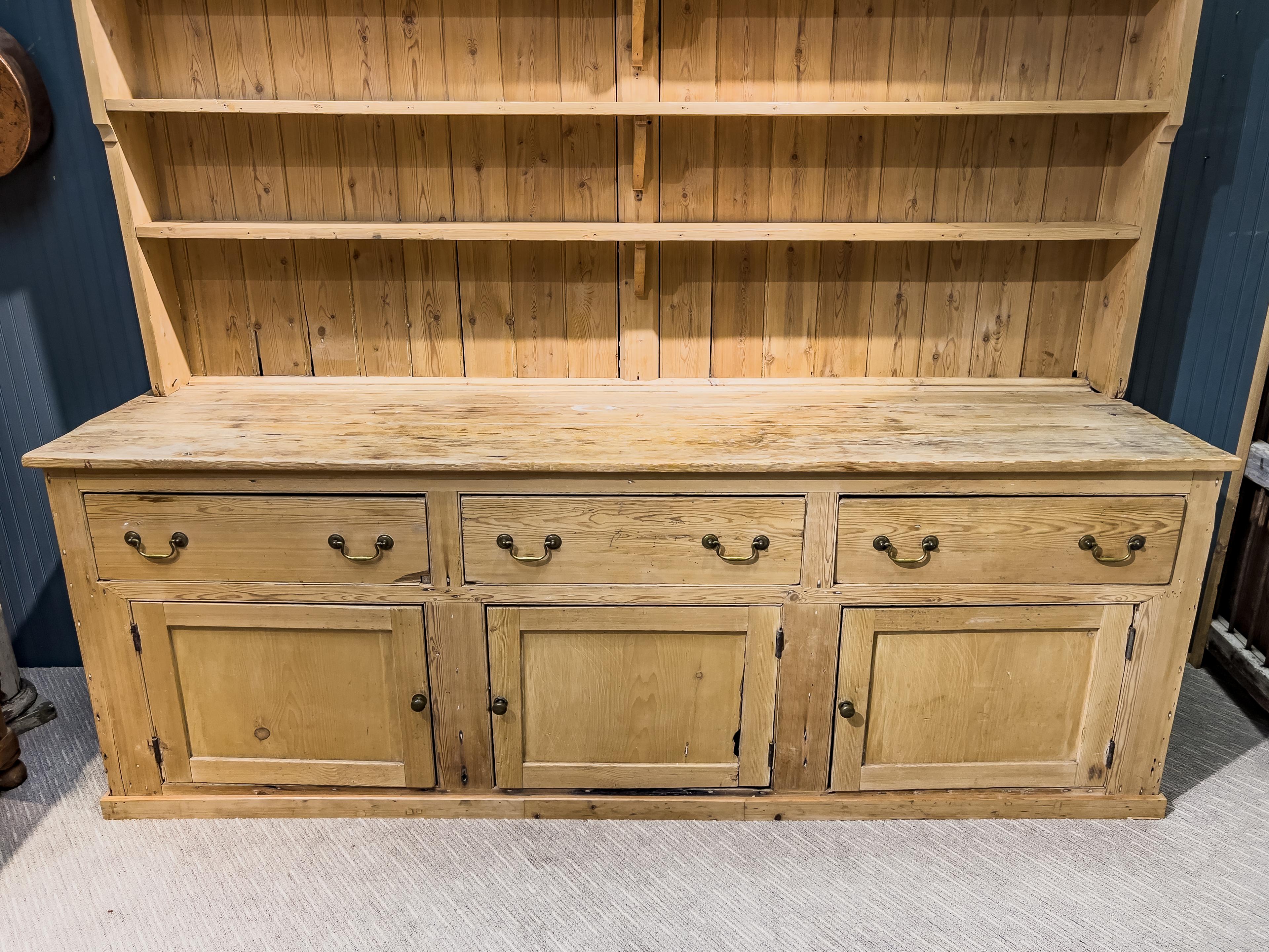 19th c. English pine dresser and Rack is a stately piece with the top portion having three shelves and the bottom having three drawers and three cabinet doors. This piece has a very large stature as it is 92 inches high and 100 inches wide.