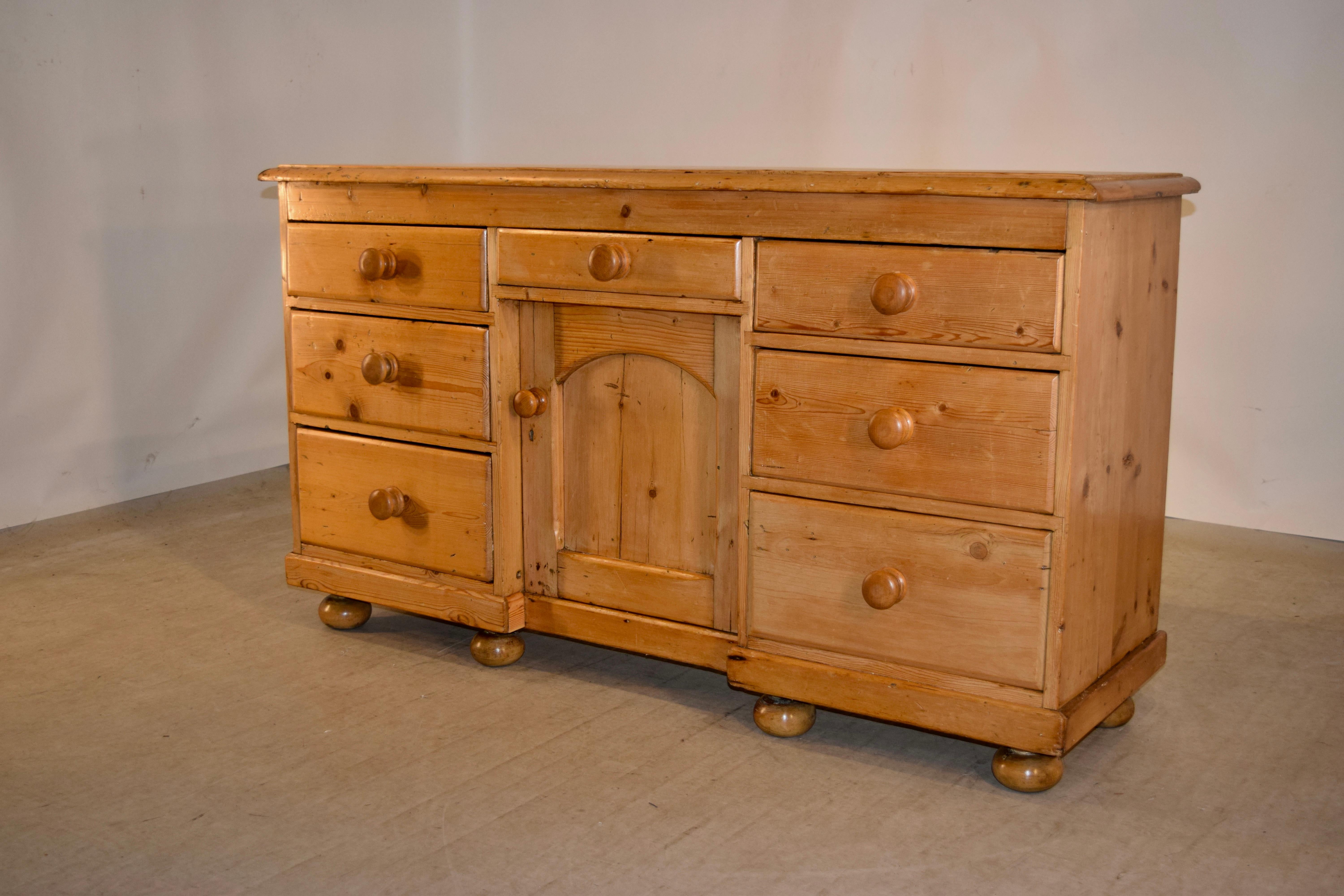 19th century pine dresser base from England with a three board top which has a beveled edge, following down to simple sides and a central drawer over a single recessed door, which opens to reveal shelving. This is flanked by two stacks of three