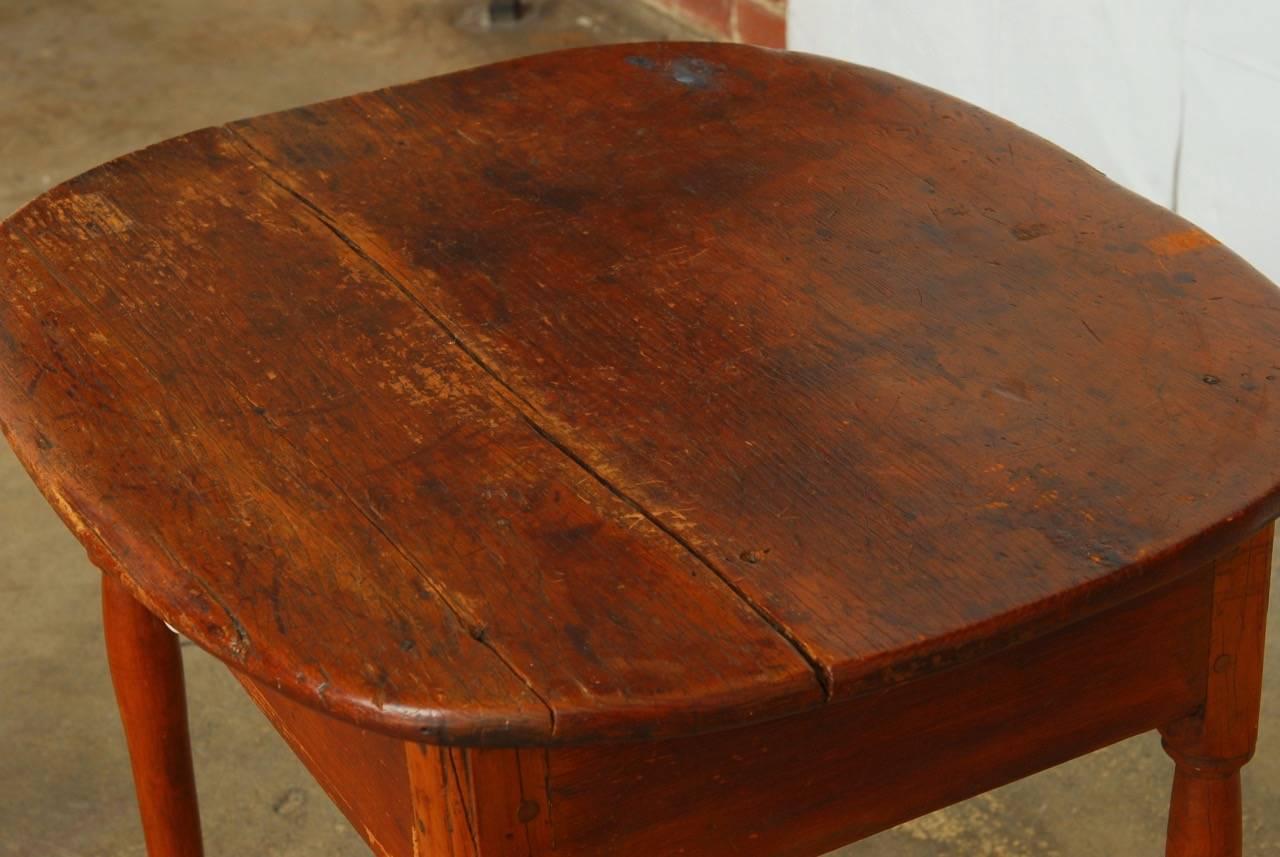 Rustic 19th century English farmhouse table constructed from pine. Fronted by a single drawer with a later porcelain knob. Features an oval work surface over the square case made with mostly wood peg joinery. Supported by elegant straight legs that