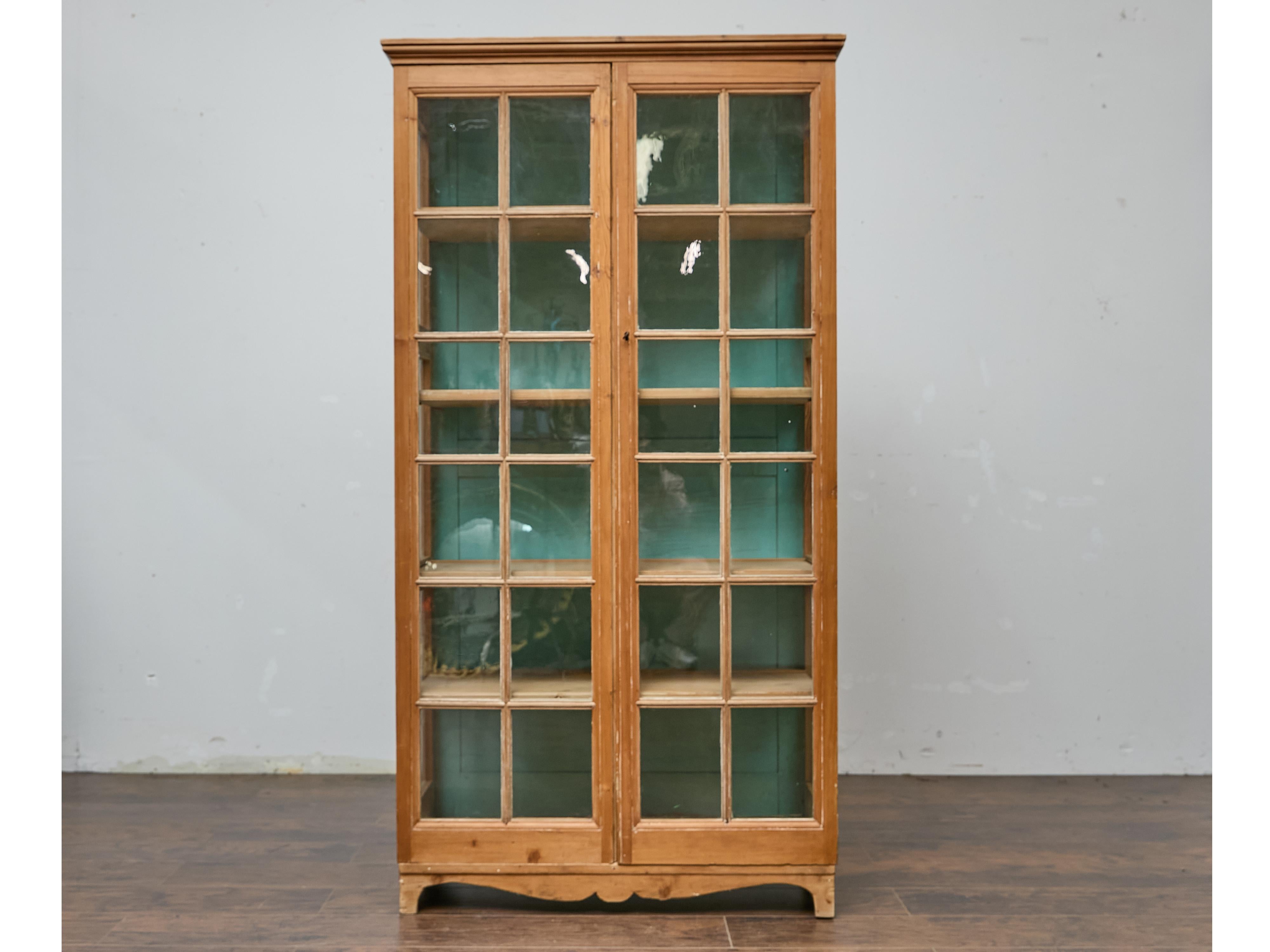 With its tall, narrow silhouette and charming paned glass doors, this 19th-century English pine cabinet invites effortless storage and display. The warmth of the naturally aged pine is enhanced by subtle wear, while the soft blue-green painted