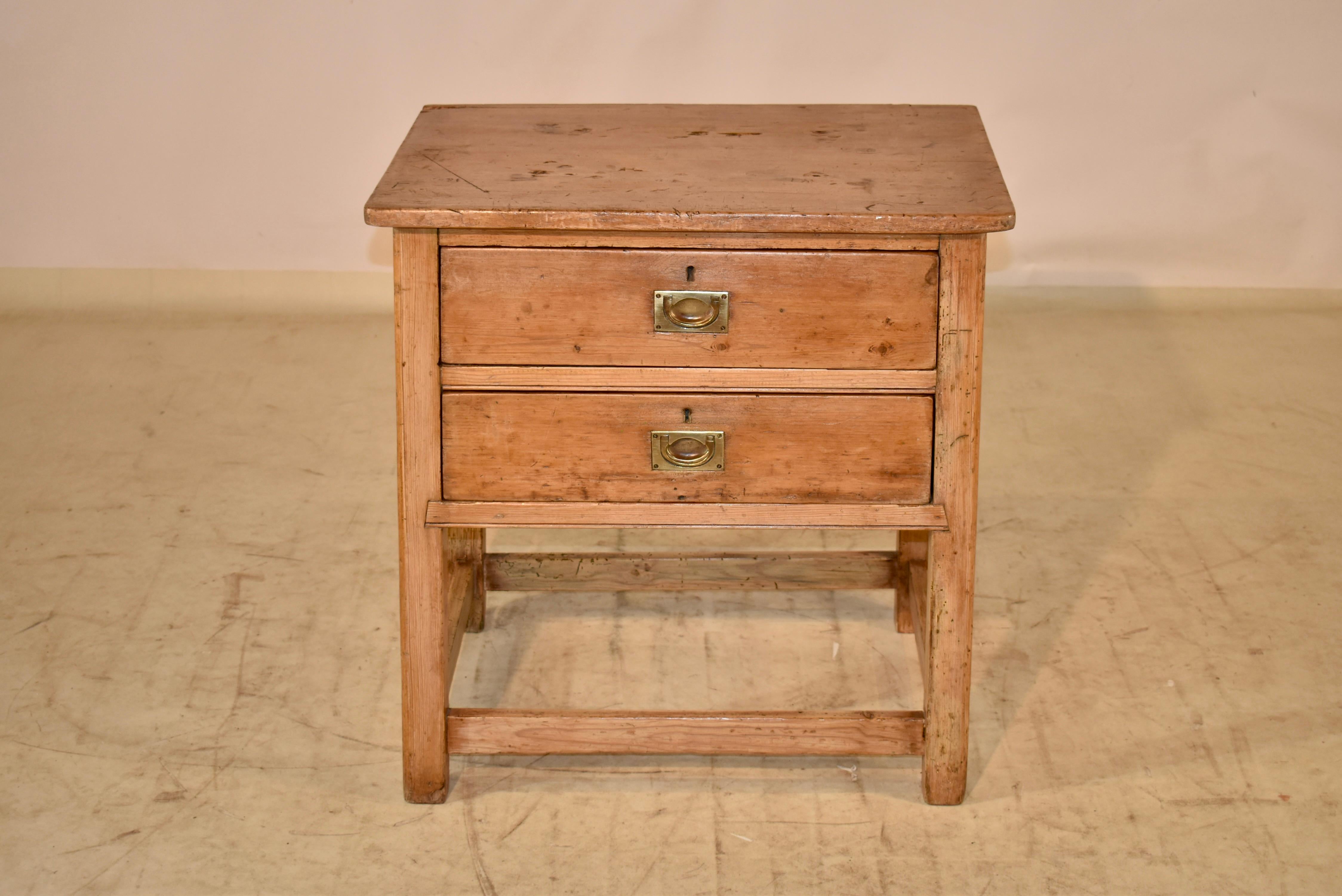 19th century Rustic pine side table from England. The top has rounded front corners, and follows down to simple aprons on the sides. The front of the table has two single drawers, both with inset brass handles. The table is supported on primitive