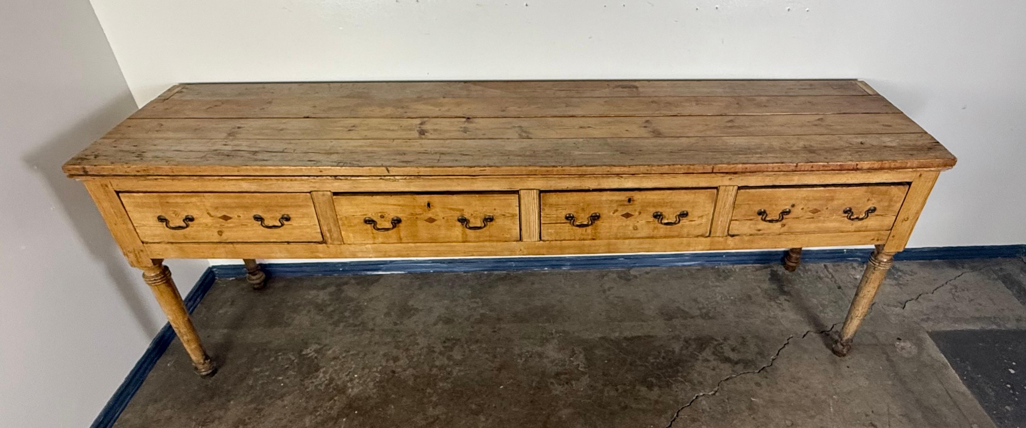 This charming 19th-century pine sideboard exudes rustic simplicity with timeless appeal. Crafted from solid pine, it features a long, rectangular top with a naturally aged surface that reveals a beautiful, weathered patina, bearing the marks of time