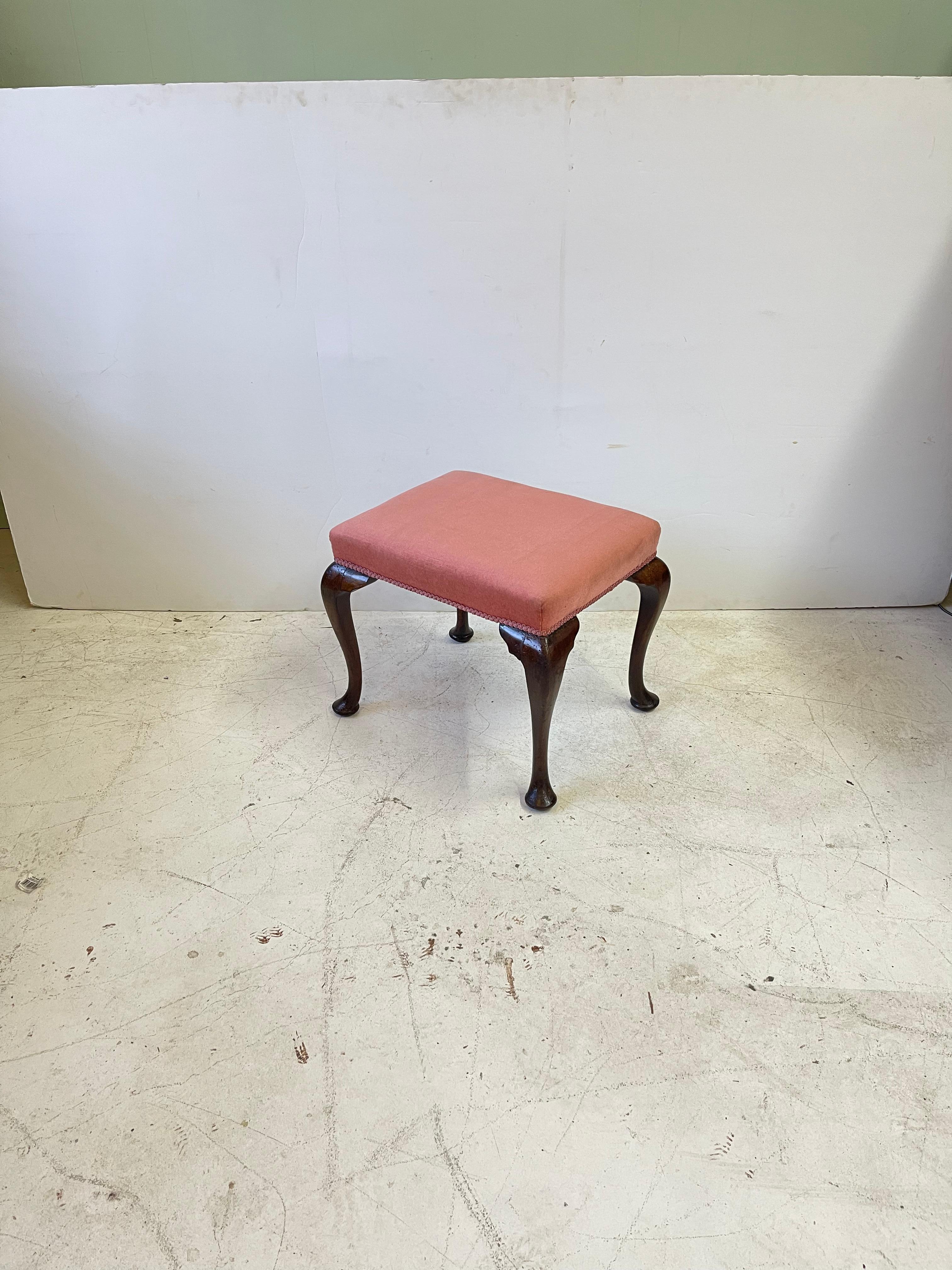 19th Century English stool of mahogany in the style of Queen Anne. The stool has a rectangular form with elegantly proportioned cabriole legs and slipper feet. The seat is currently upholstered in a pink velvet fabric and matching trim. This classic