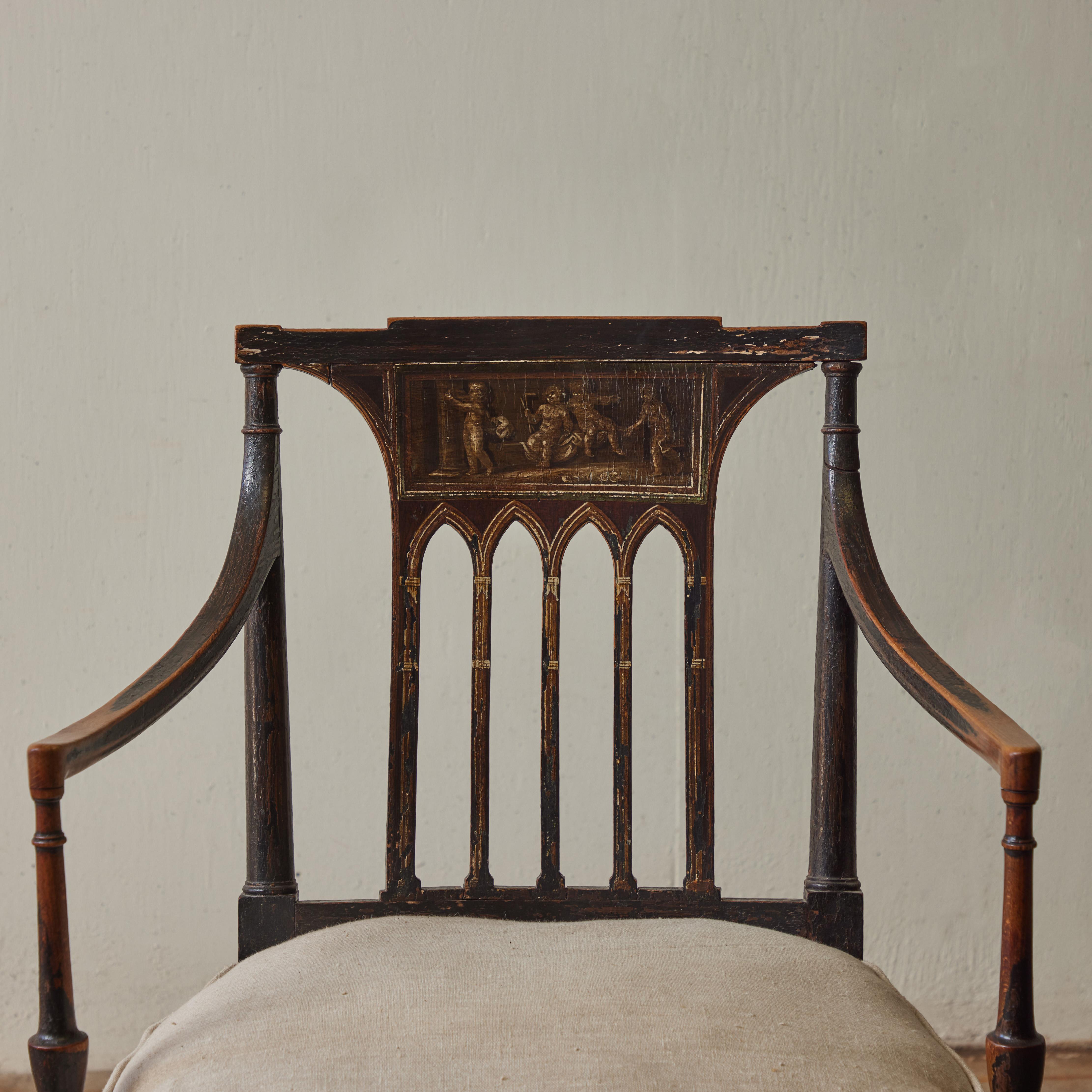 Early 19th century English espresso black caned seat armchair in the Regency style. Featuring a gilt neoclassical motif of dancing cherubic figures and a contemporary Belgian linen cushion, this handsome yet delicate accent chair adds a uniquely