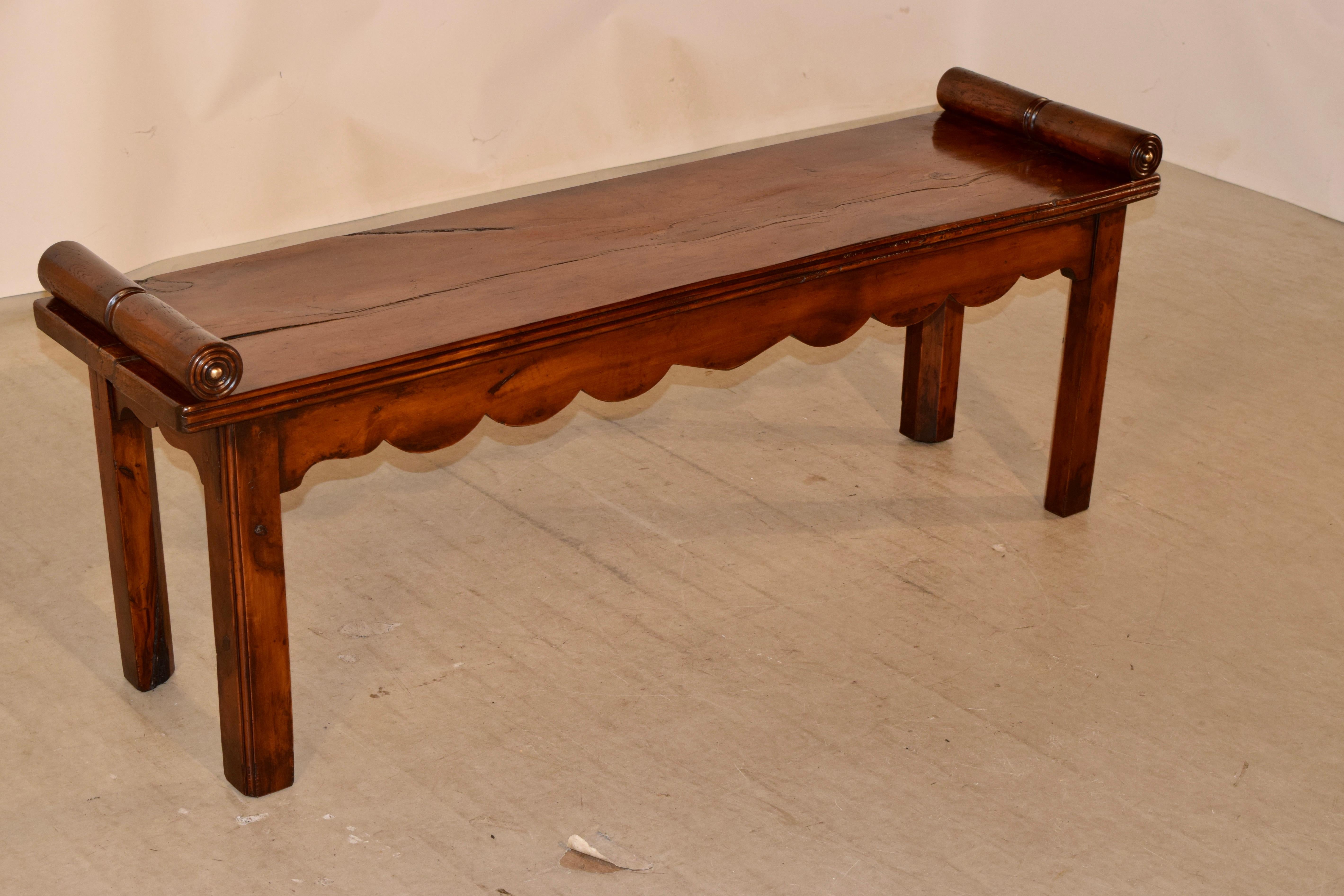 19th century English bench made from pecky cypress. The bench is in an elegant Regency form with hand turned rolled arms over a single plank seat with a molded edge and a scalloped apron on one side and a simple apron on the other. The bench is