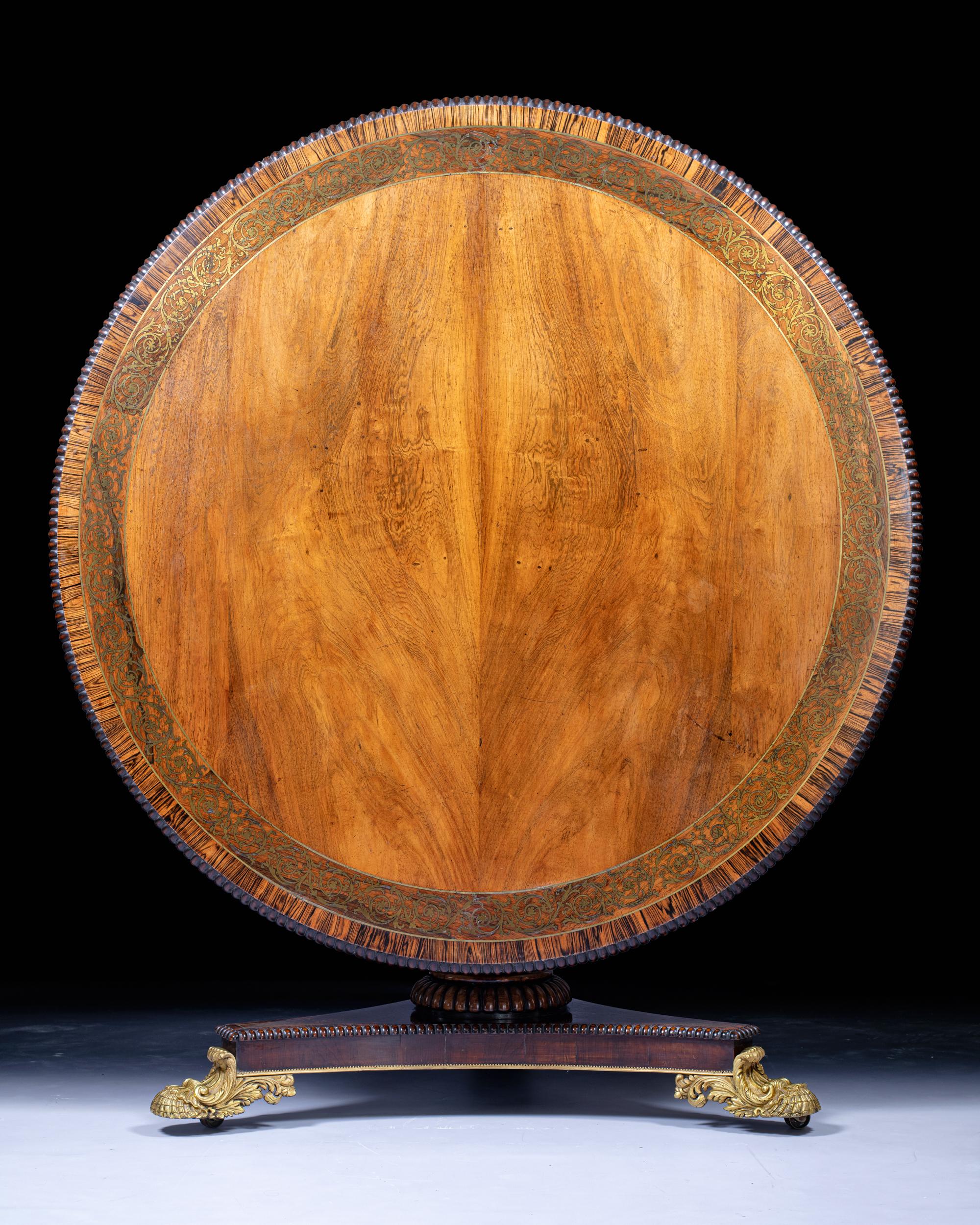 An exceptional early 19th century English Regency centre table, the circular tilt top having radially magnificent figuring and colour,  bordered by intricate brass inlaid, with Zebra wood banding and gadroon edge, supported by a turned, ringed,