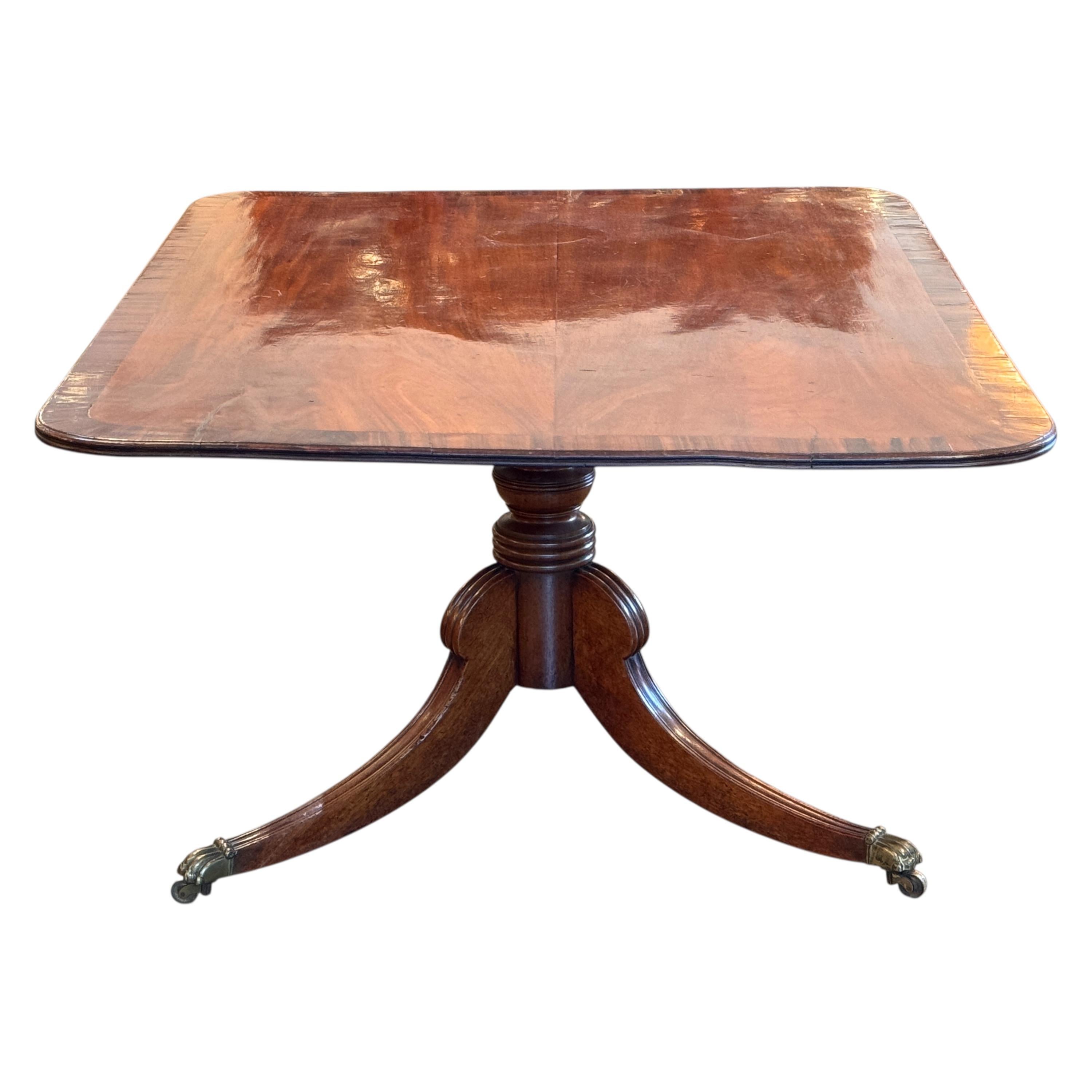 Tavolo da colazione a ribalta della Reggenza inglese risalente al XIX secolo, con piano impiallacciato in mogano riccamente figurato e bordo a reticolo su una base a piedistallo tornita. Le gambe a treppiede terminano con CAP e rotelle in ottone,