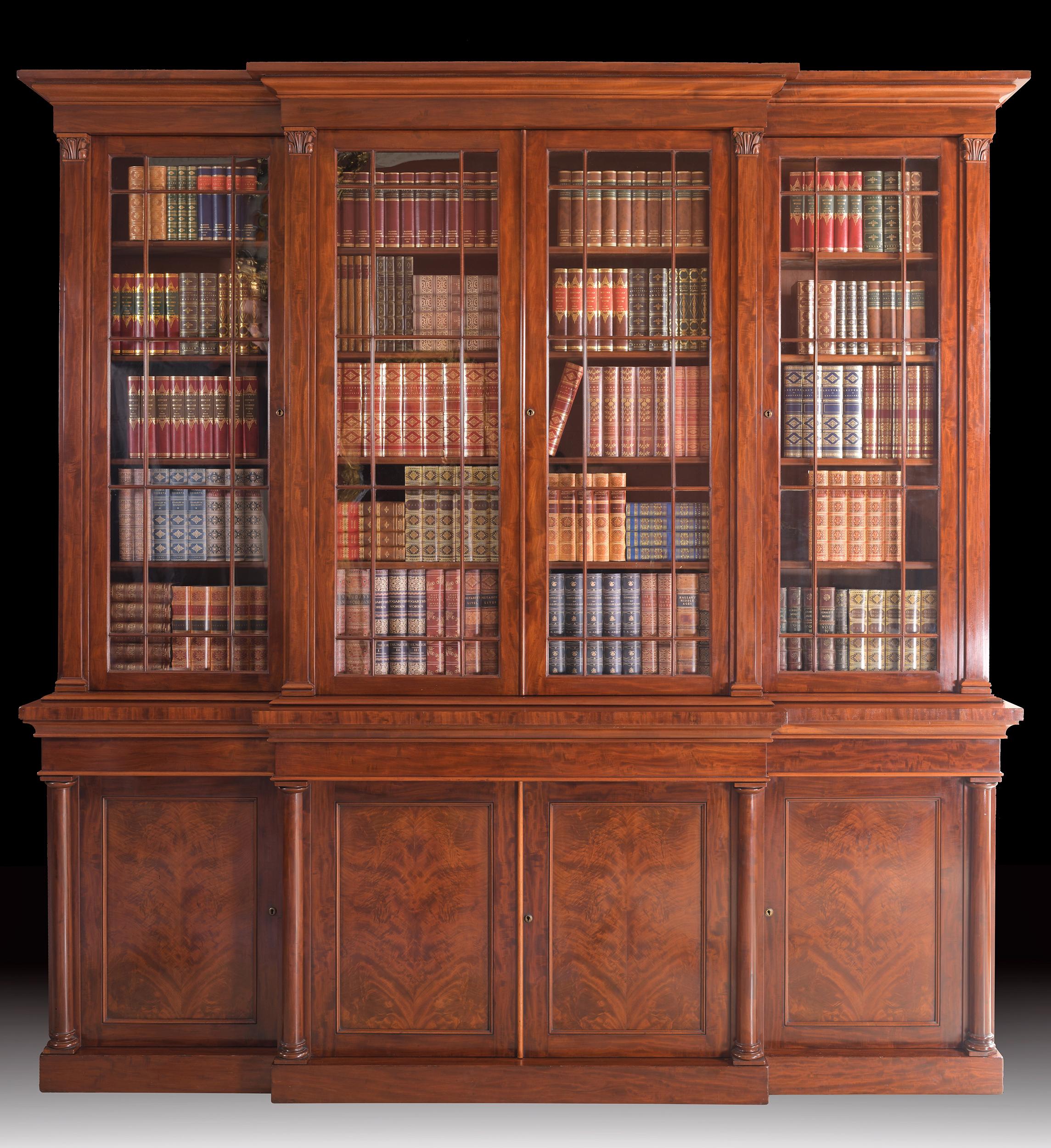 A superb Regency flame mahogany four door breakfront bookcase attributed to Gillows of Lancaster, surmounted with pierced lattice work, cresting above four geometric glazed doors, with shelved interior over four fielded cupboard doors and outset