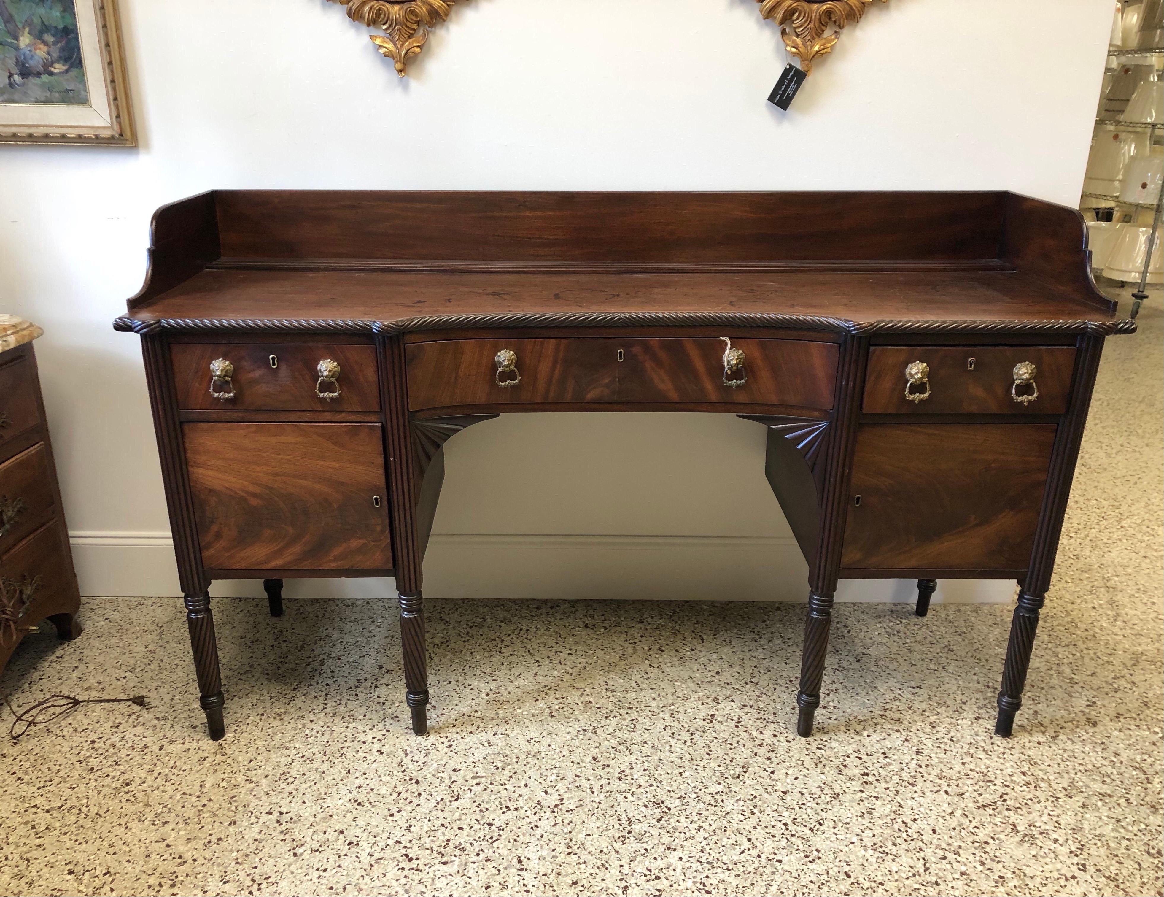 19th century English Regency carved mahogany sideboard. Shaped top with rope twist edge and backsplash. Concave center drawer with fan spandrel apron, flanked by single drawer and cabinet on each side. Reeded stiles, ring turned spiral legs ,