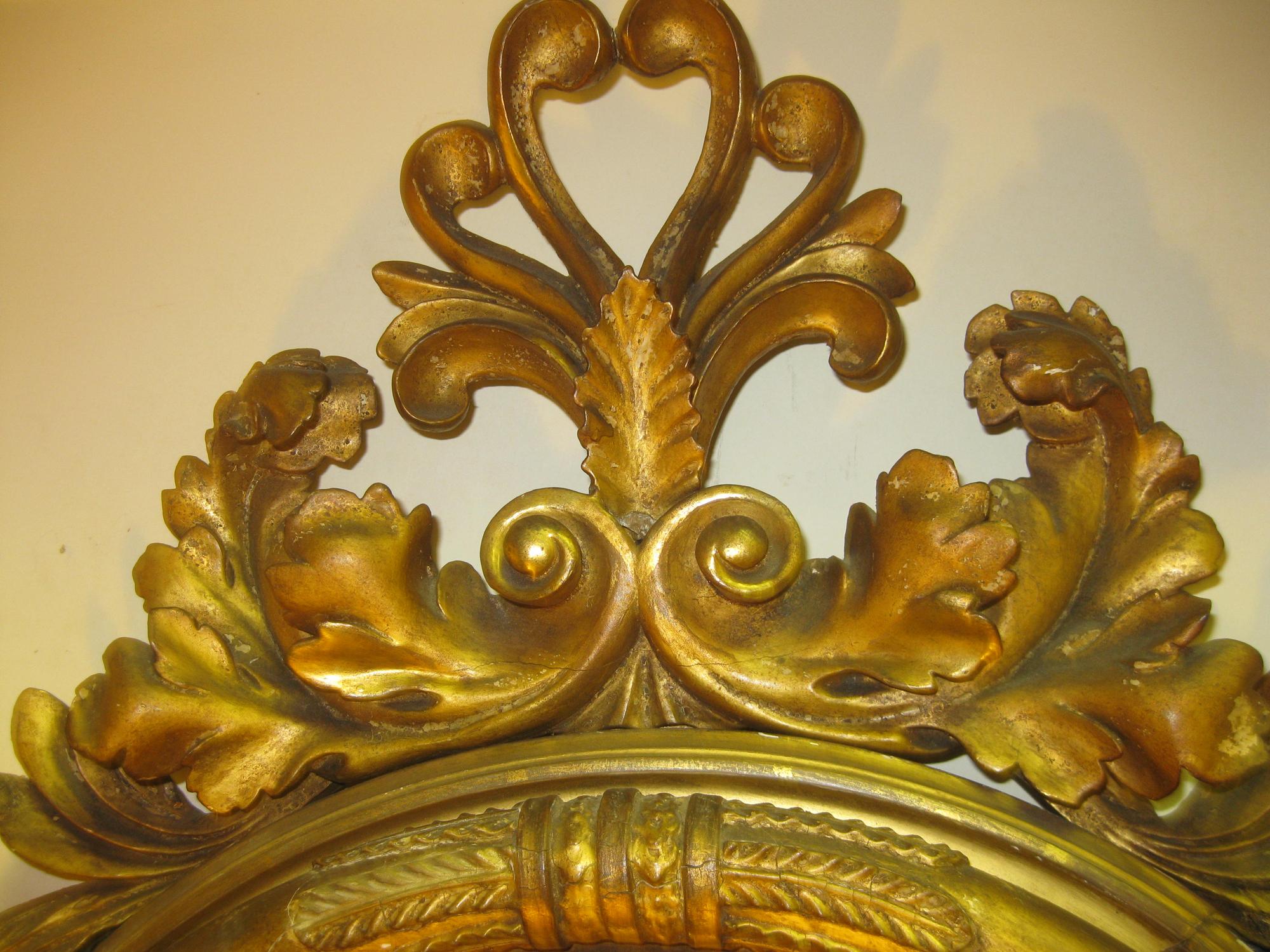 English Regency giltwood convex mirror, circa 1810. Featuring elaborate carving at top and bottom of acanthus leaves and scrolls, with two single graceful girandole. Bull's-eye mirrors first became popular in Europe during the 17th and 18th