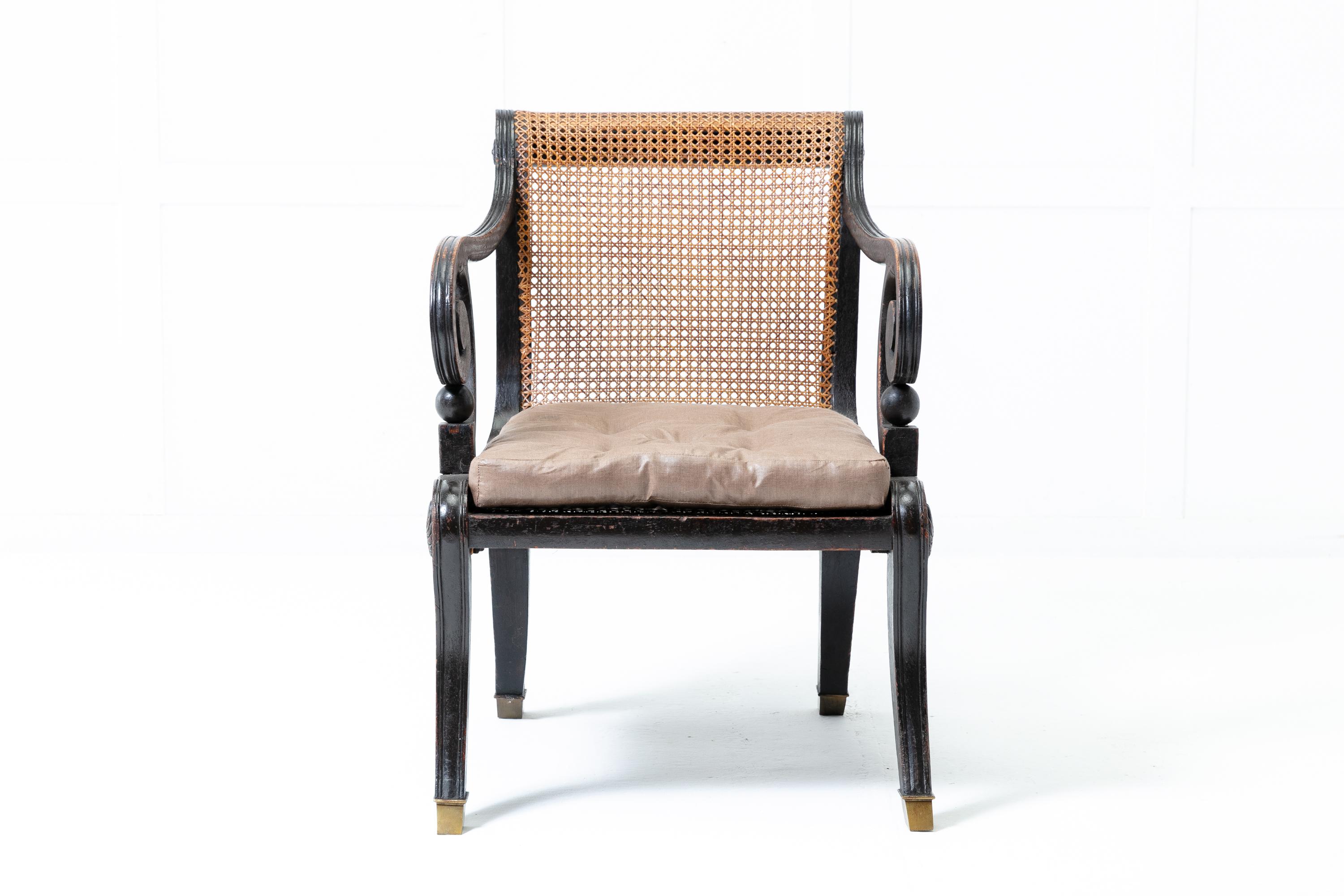 A great shaped Regency ebonised library chair, circa 1820 with its original ebonised finish. Having an exaggerated scroll back and arms. The reeded frame is caned and decorated with carved paterae to the sides. Standing on sabre legs with brass