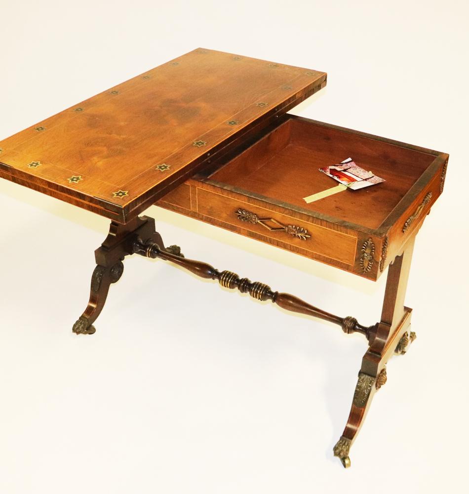 19th century English Regency games table, with fold-over inlaid top. Inlaid brass and walnut raised star decorations, and inlaid banding throughout, as well as gilt-bronze decorative mounts, with carved trestle legs and turned stretcher, 29