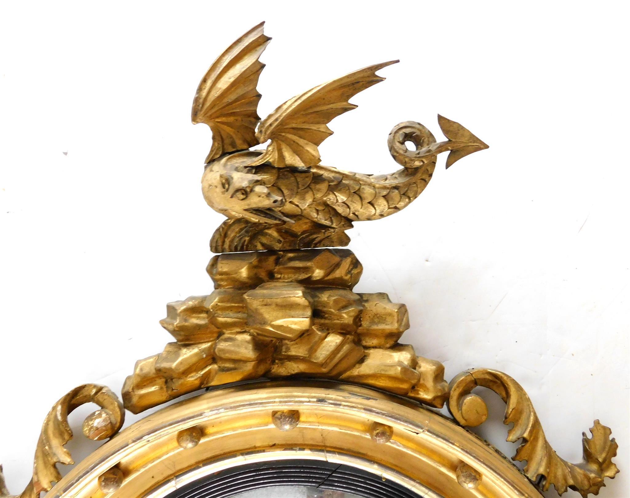 Ancien miroir convexe en bois doré sculpté de style Régence anglaise, datant d'environ 1820.
Le miroir convexe est entouré d'une élégante baguette ébonisée et d'une frise moulurée en bois doré avec des montures en forme de boules. Le pendentif