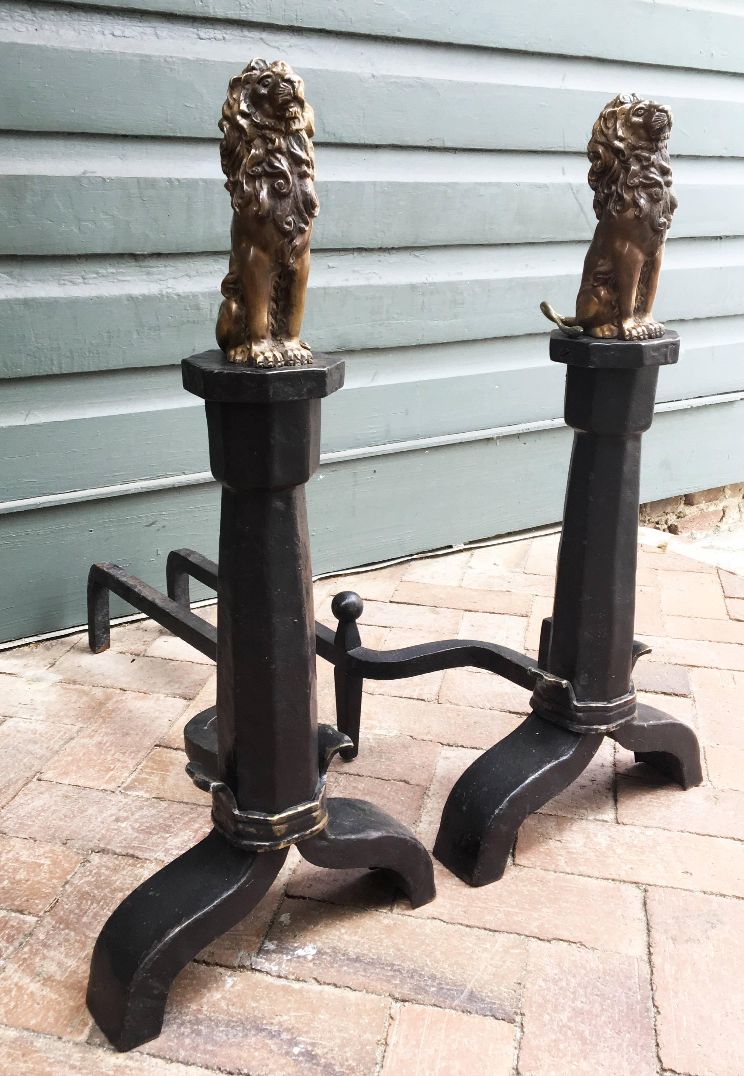 This beautiful pair of English Gothic Revival andirons with true bronze lions sitting on wrought iron octagonal plinths with bronze wrap belt at base terminating into iron scrolled feet.