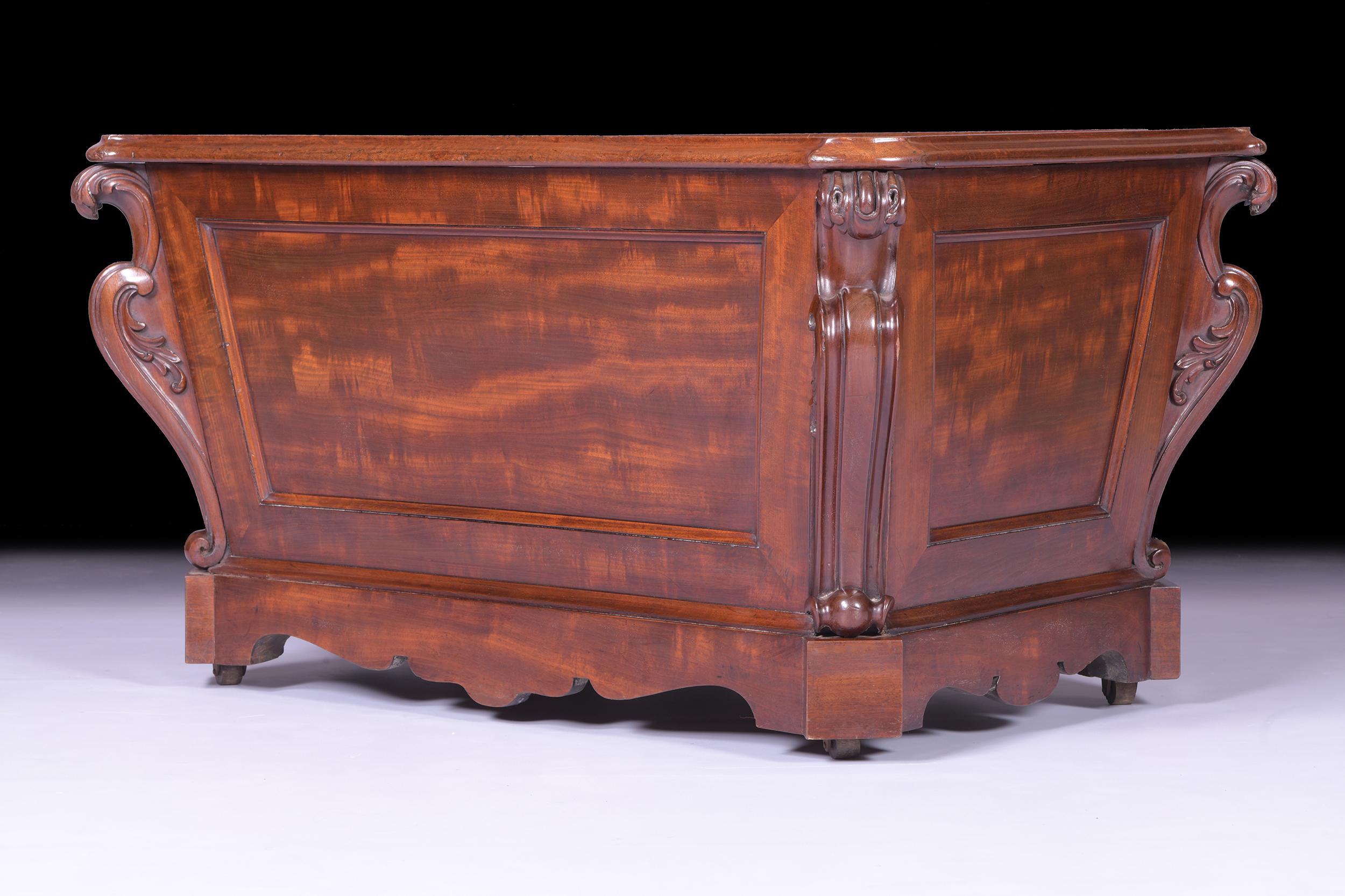 A fine early 19th Century English Regency mahogany open cellarette attributed to Gillows of Lancaster, of open sarcophagus form with an overhung and carved top edge over panelled sides, with carved scrolling corners raised on Cope's patent brass