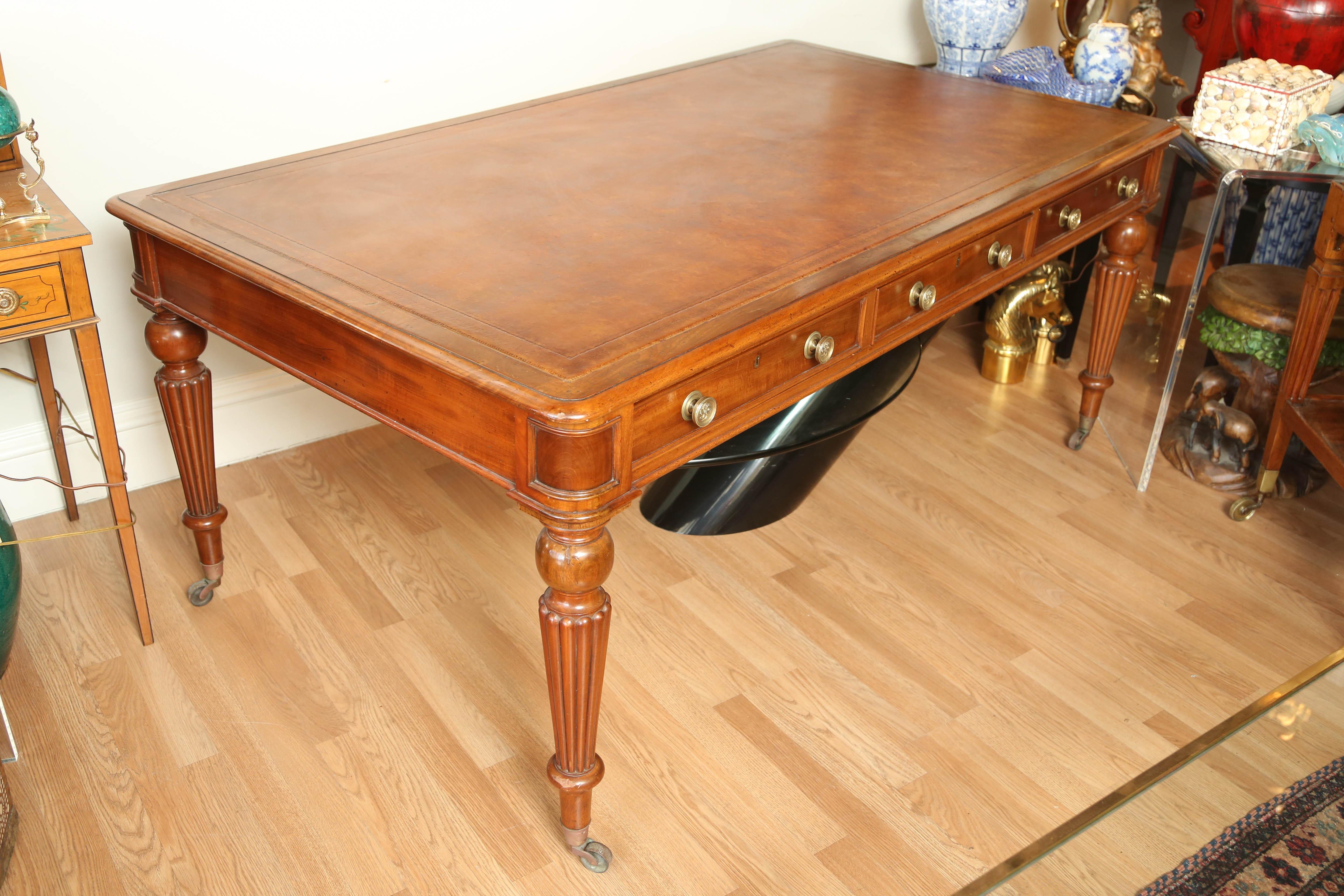 Grand English Regency period mahogany partners desk with three drawers on each side. Original brass hardware and handsome leather work surface. Detailed tapered legs with brass castors.