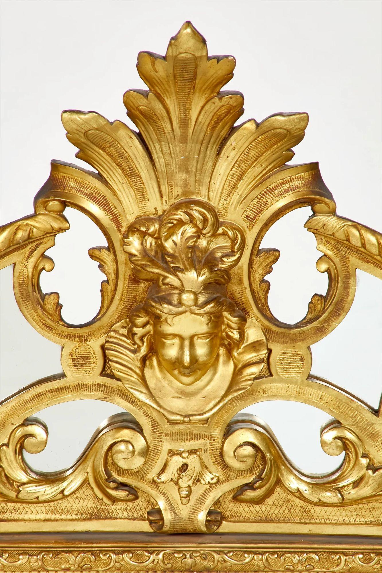 Regency style hand-carved giltwood mirror made in England in the 19th Century; having a focal point of a female espagnolette mask above a rectangular bevelled plate within mirrored borders. The piece is adorned with scrolling foliage all