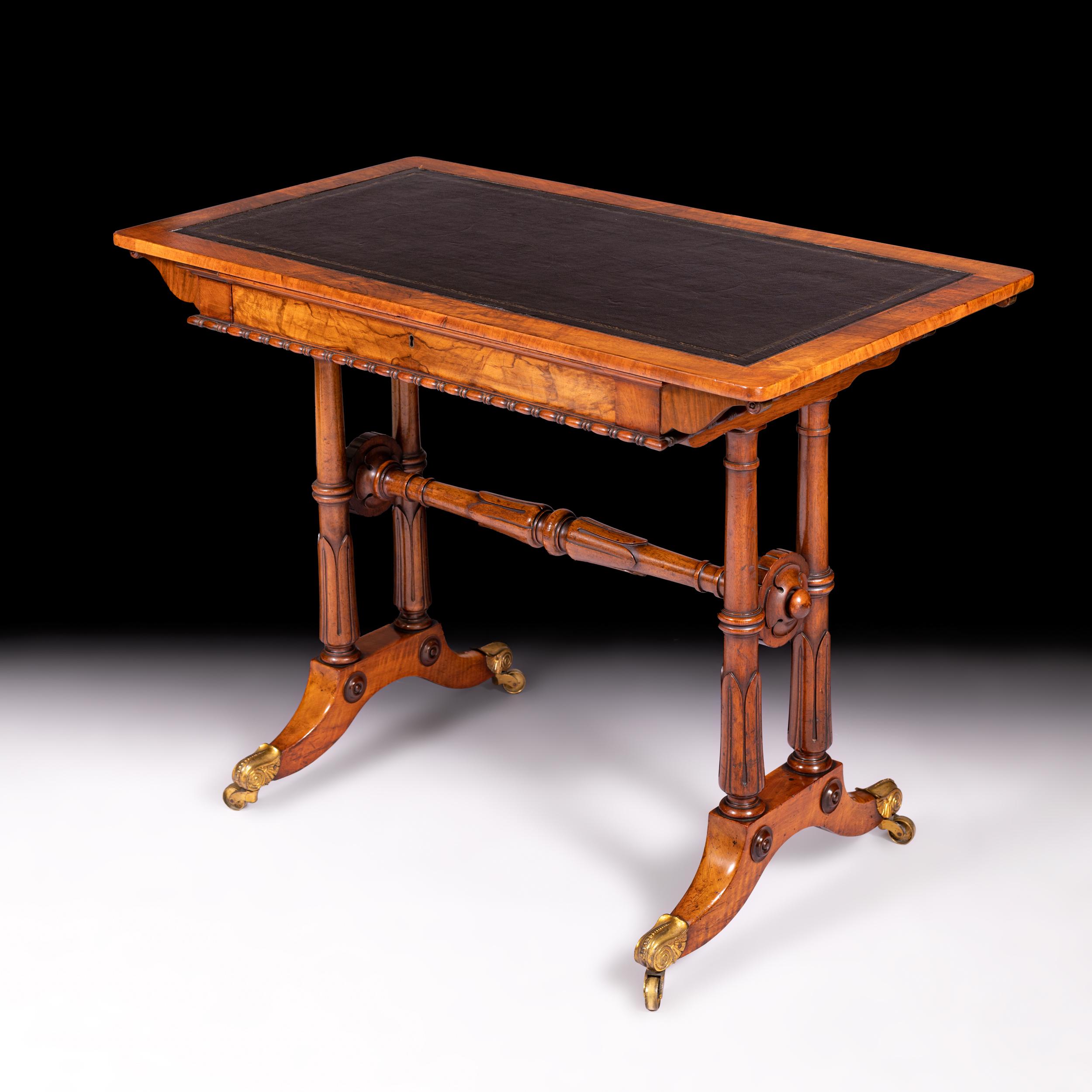 A George IV walnut rectangular writing table, the top with inset leather scriver above a shaped frieze drawer, raised on pairs of turned side supports with lotus collars and stretchers, on outswept legs with brass toe caps and castors.

Circa