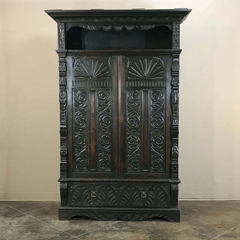 19th century English Renaissance armoire, wardrobe, cabinet features stately architecture and intriguing heavily carved embellishment and molding that includes a display shelf at top, spacious cabinet in the middle, and a full width drawer at the