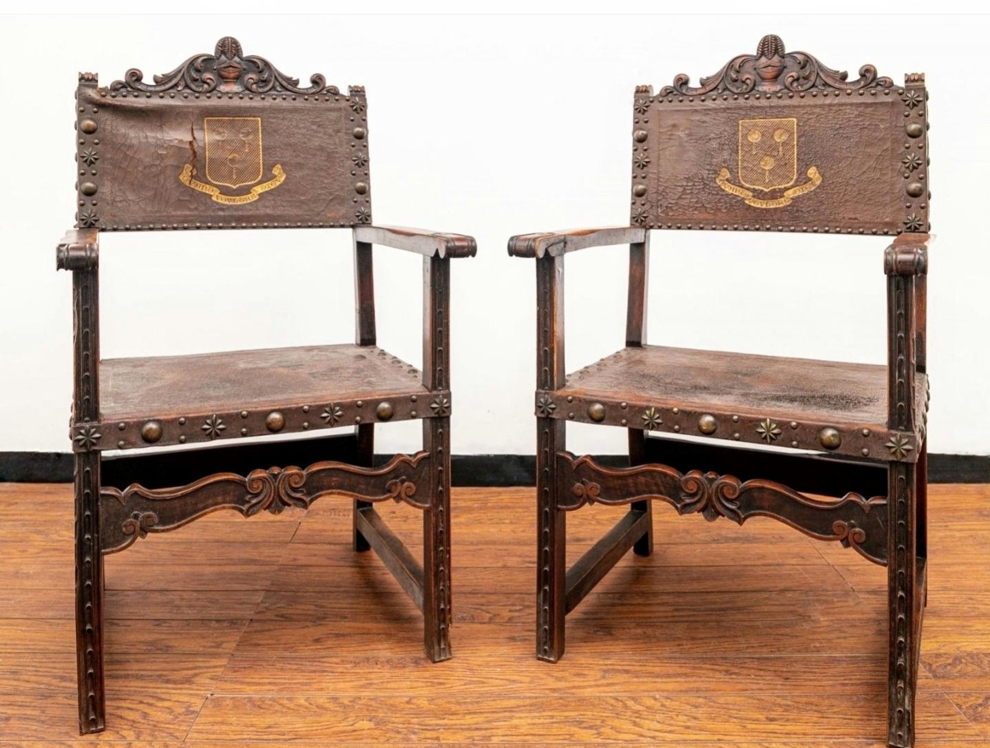 Paire de chaises d'entrée en cuir et en noyer de style Renaissance anglaise.

19e siècle, îles britanniques. Le dossier est orné d'un écusson familial doré et d'une bannière à enroulement avec inscription en latin.

Fauteuil trône médiéval européen