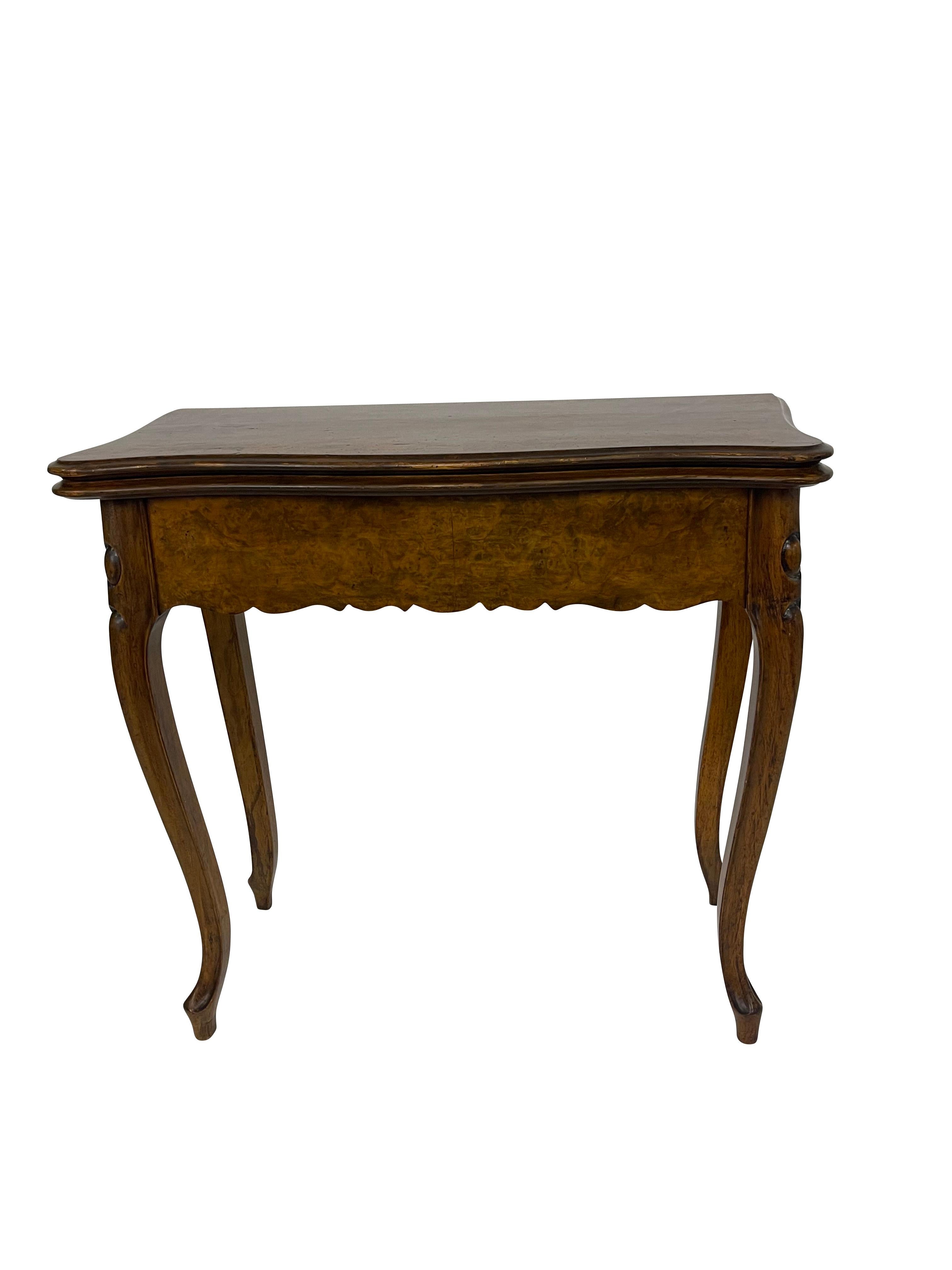 ROCOCO REVIVAL BURL WALNUT GAMES TABLE English, Mid to late 19th Century. The serpentine hinged top swivels and opens to a baize-lined playing surface, above a scalloped skirt, on cabriole legs ending in pointed-shaped feet—lightweight, compact