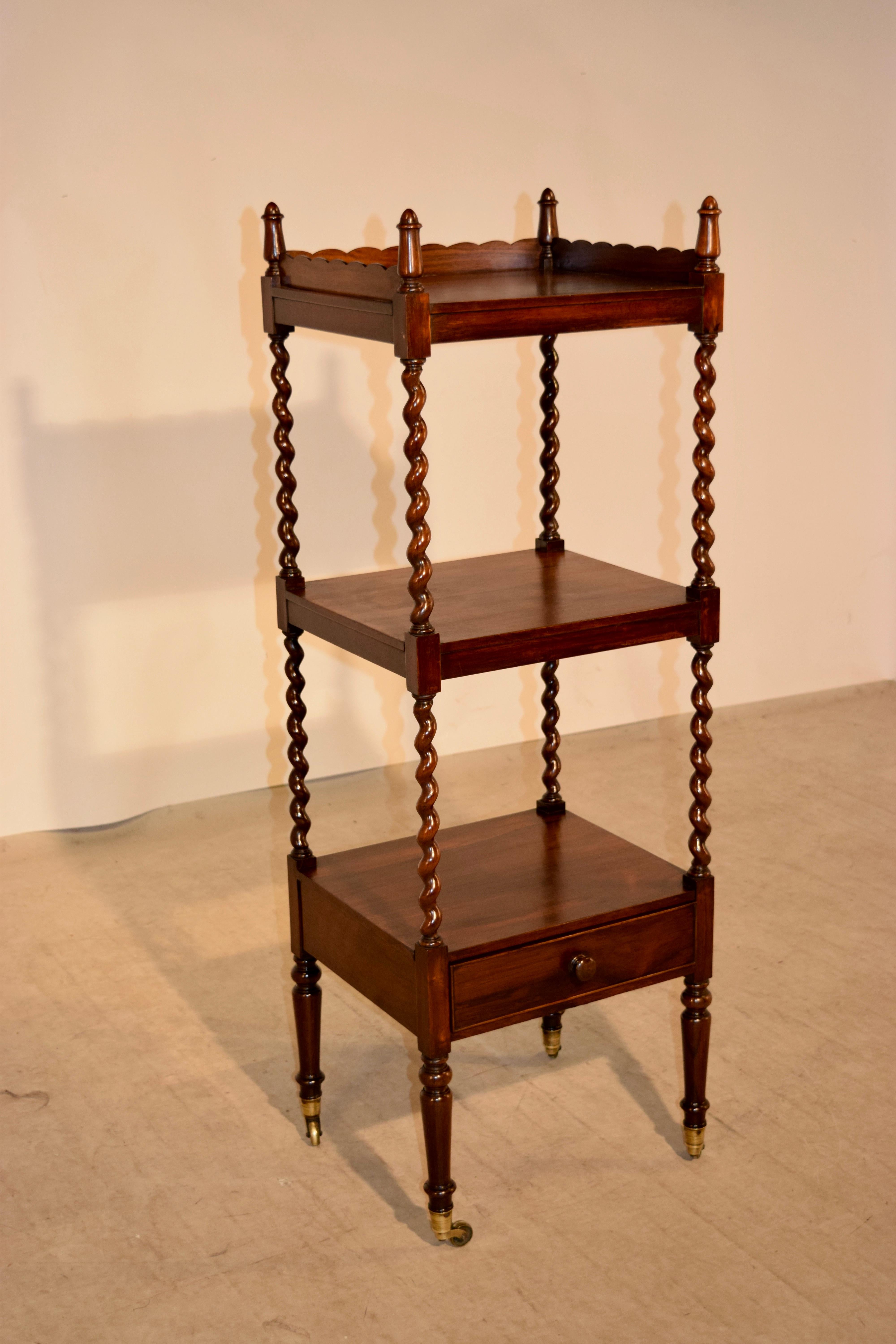 19th century English étagère made from rosewood. The top is decorated with finials and a lovely scalloped gallery following down to three shelves, separated by hand-turned barley twist shelf supports. The third shelf has a drawer below. The piece is