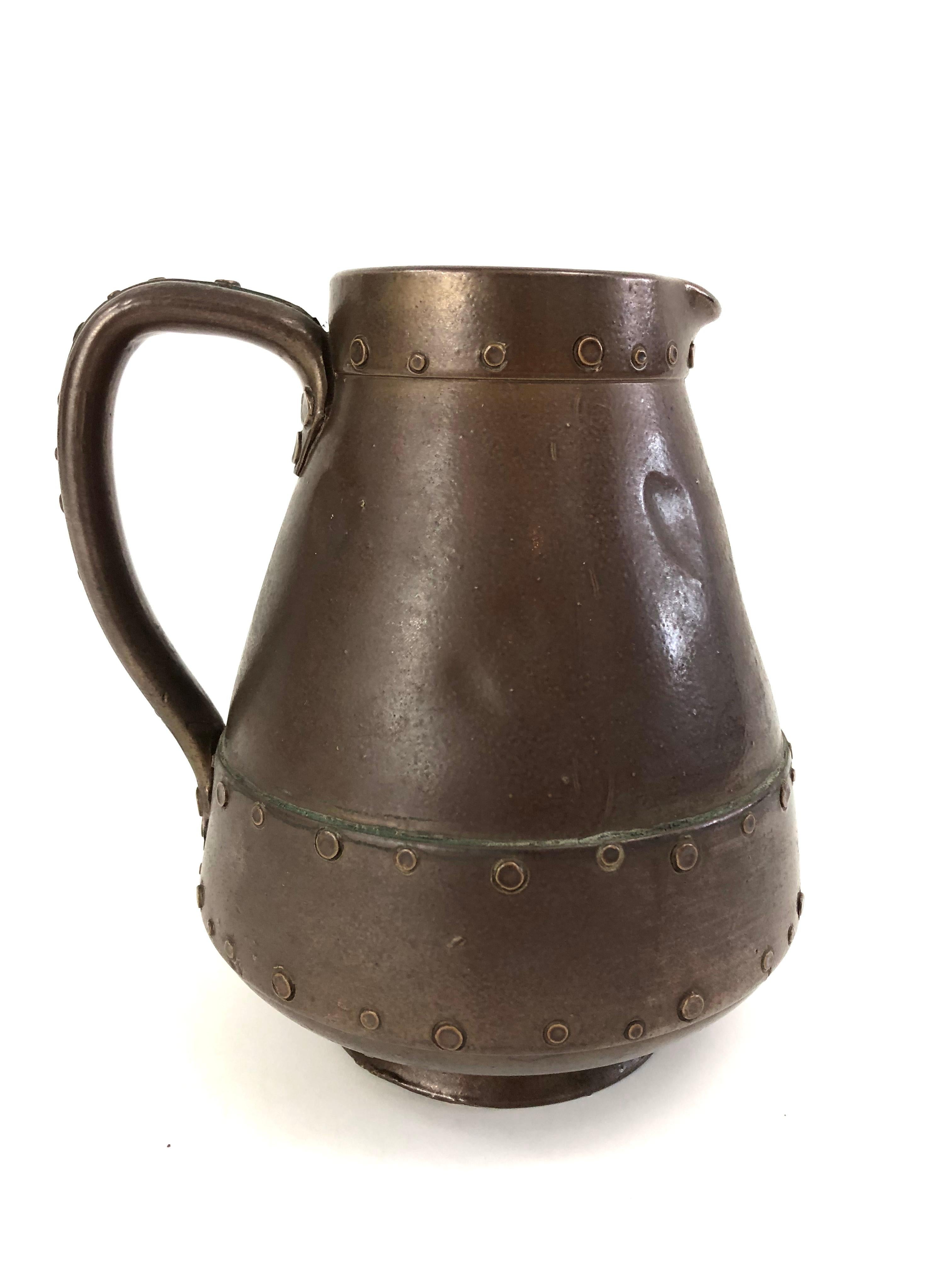 A beautifully and inventively made English Royal Doulton trompe l'oeil pottery pitcher, English, circa 1880, made of glazed ceramic, but designed, in every detail, to resemble a copper pitcher. From its perfectly crafted rivets and the appearance of