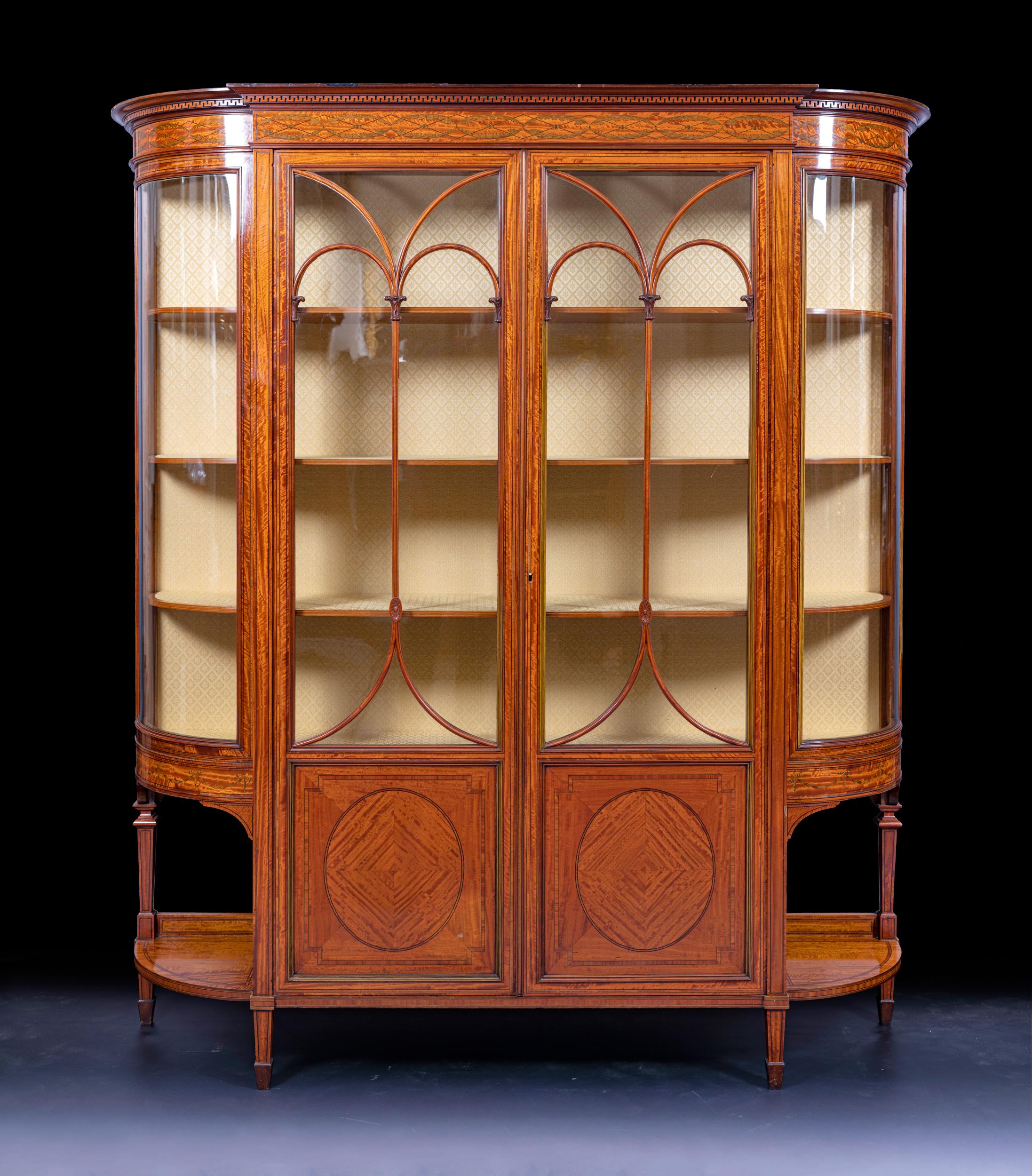 A stunning quality satinwood display cabinet by Holland & Sons, the D- shaped outline form having moulded cornice above string inlaid frieze over a pair of glazed doors above fielded panels enclosing a lined interior with 3 shelves, all flanked by