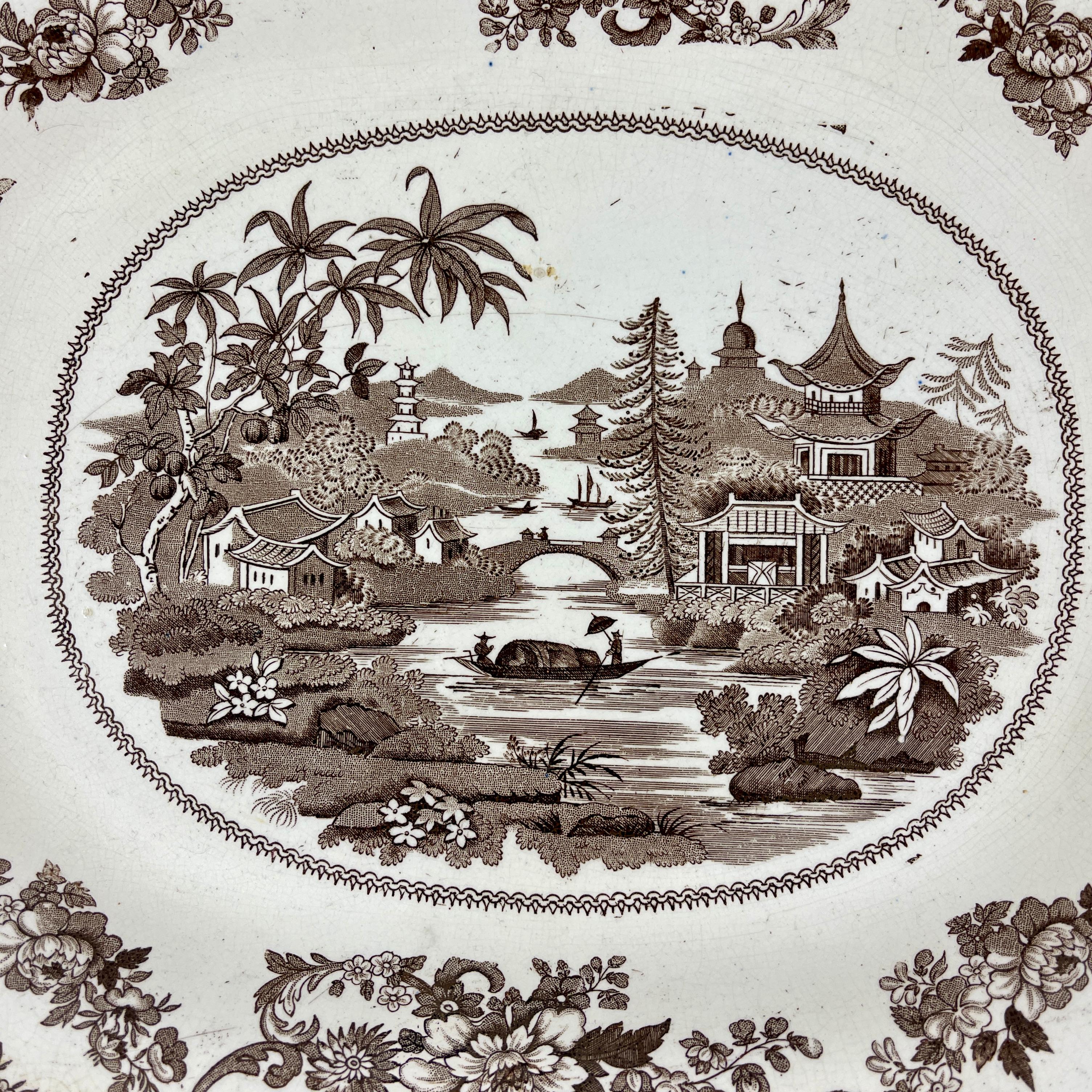 From the Staffordshire pottery region of England, a sepia tone transfer printed shallow bowl or deep platter, maker unknown, circa mid 19th century.

A central Chinoiserie inspired pattern showing a landscape of Pagodas, bridges, and a boat on the