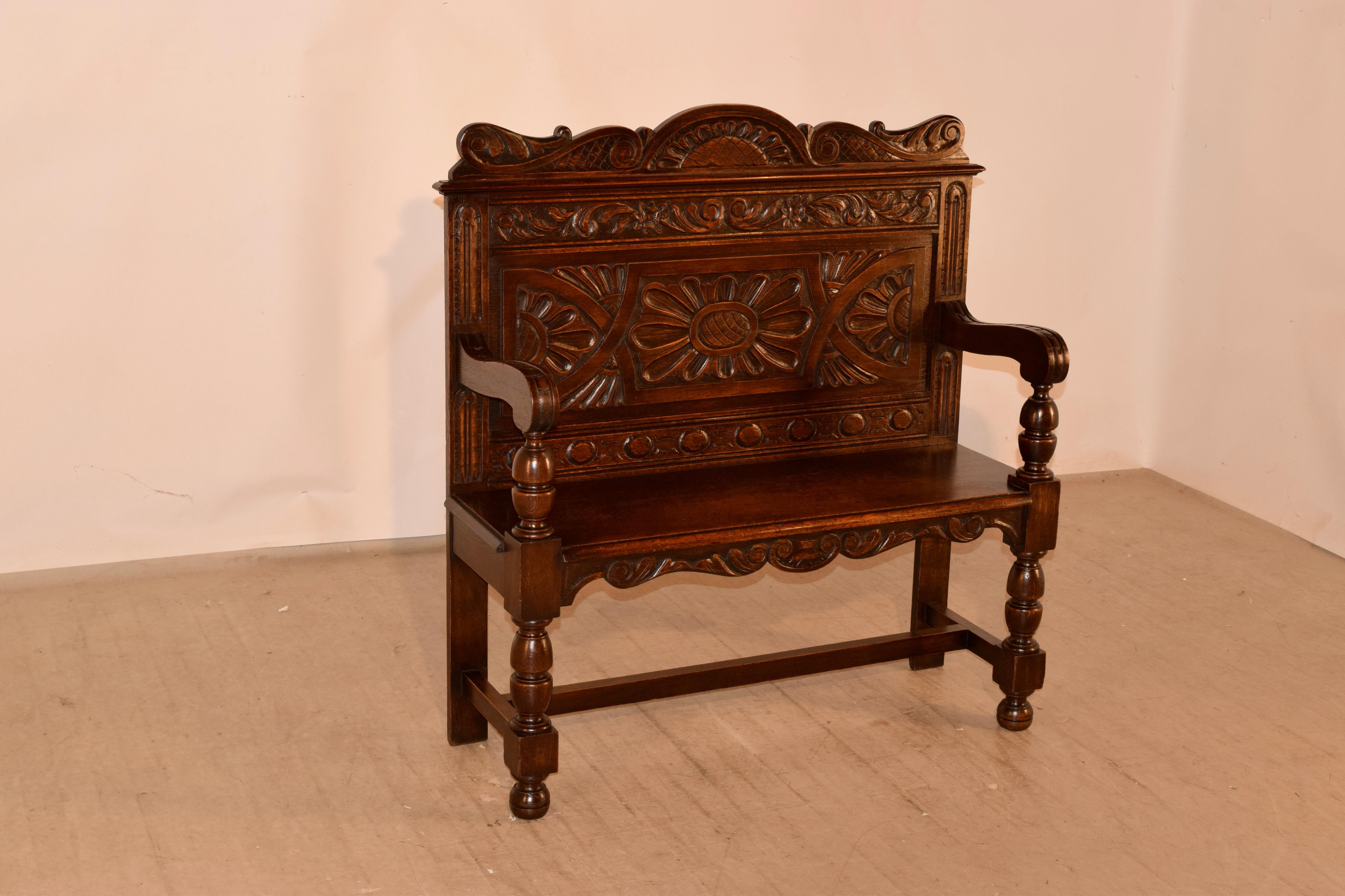 19th century oak settle from England. The top has a lovely scalloped and hand carved decorated crown over a wonderfully hand carved decorated paneled back. The arms have scrolled ends over hand turned supports, which continue to the front legs. The