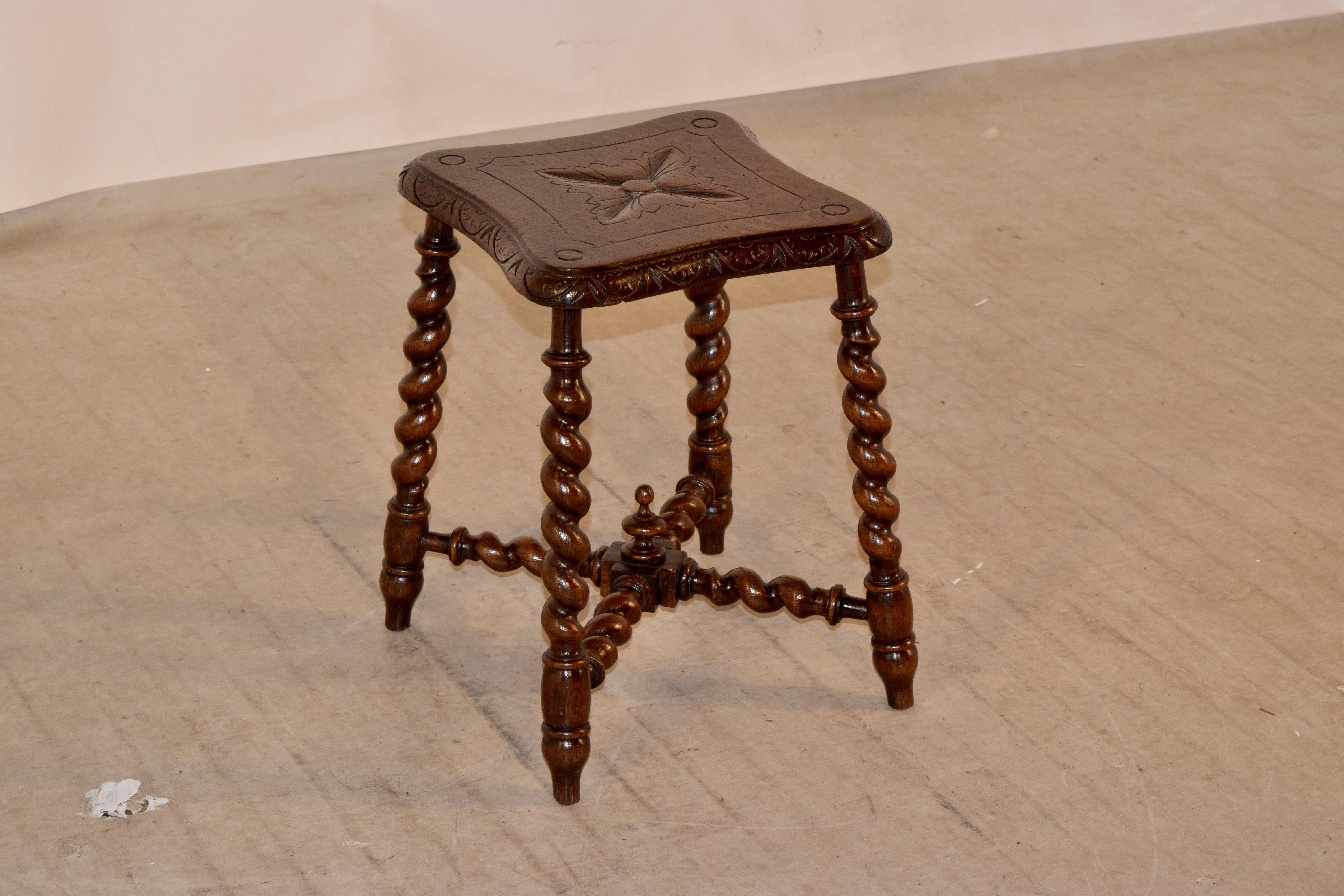 19th century oak stool from England with a shaped top which has a beveled and carved decorated edge and carved decorated top. The legs are hand turned barley twist, and are joined by matching stretchers, decorated with a hand turned finial.