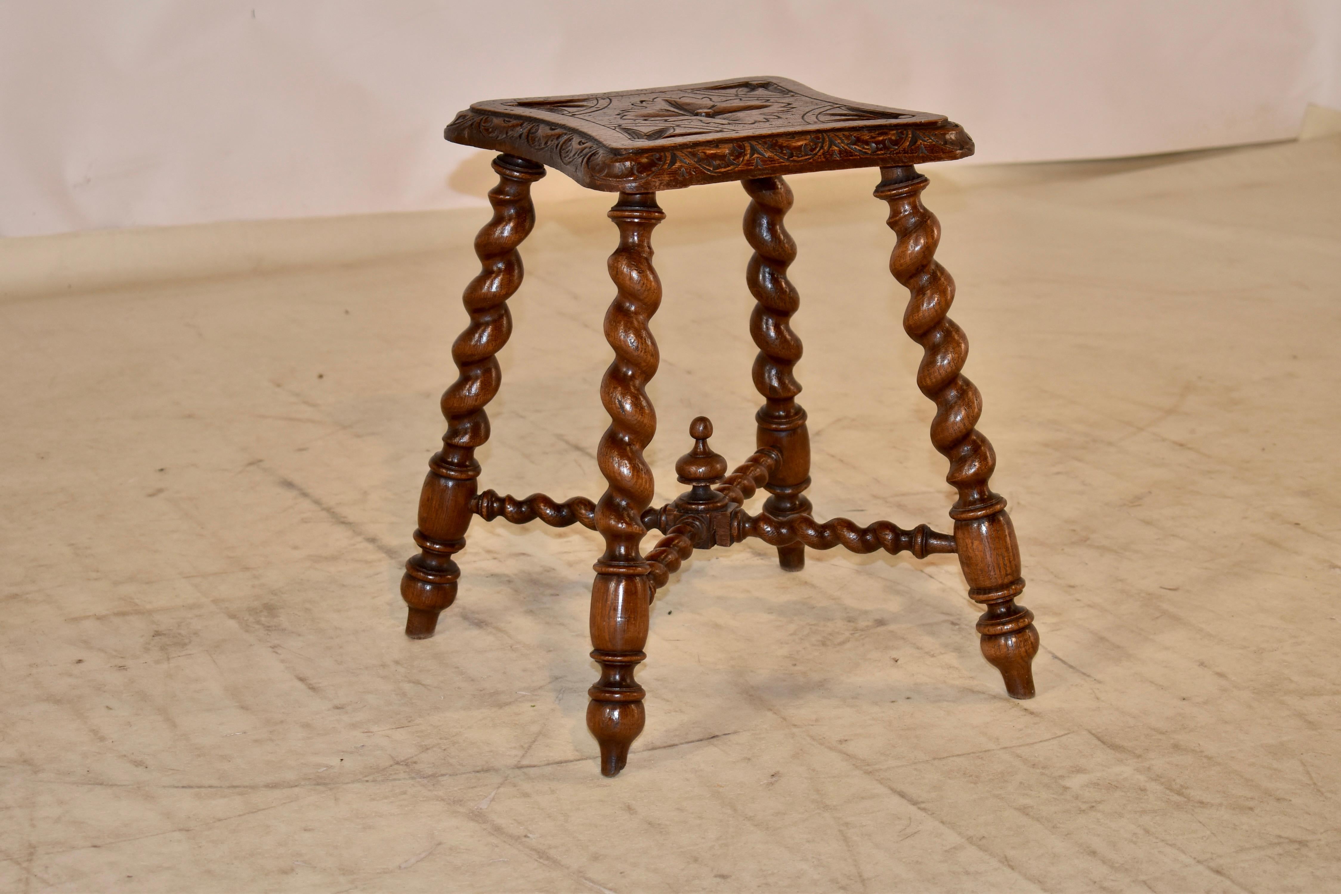 19th century Oak stool from England with a shaped top which has a beveled and carved decorated edge and carved decorated top. The legs are hand turned barley twist, and are joined by matching stretchers, decorated with a hand turned finial.
