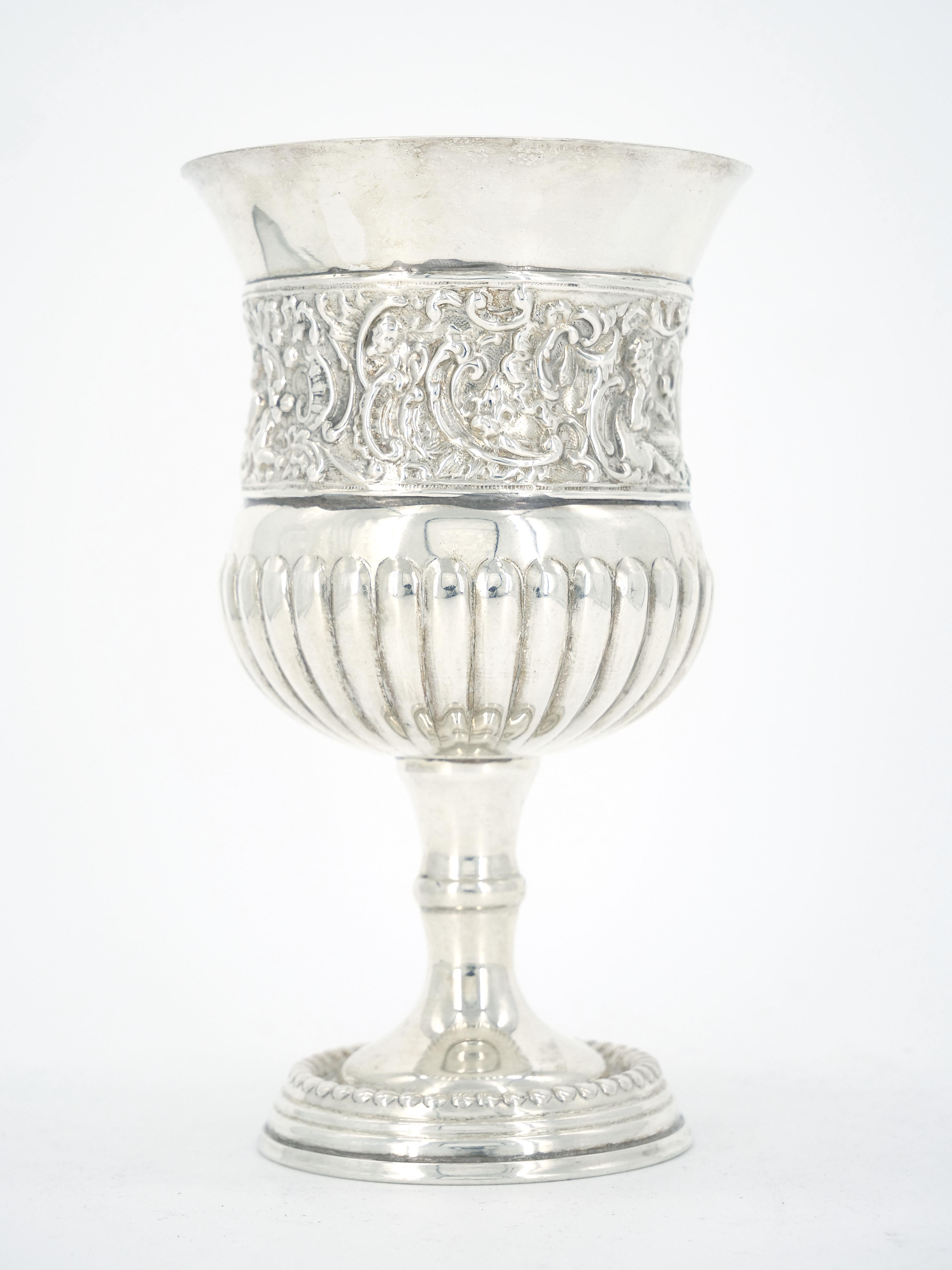 Nineteenth century silverplate wine goblet with beaded round foot, gadrooning below a pinched waist featuring an ornately chased band depicting figures, foliate and rocaille motifs, and a flared rim. Signed underneath with two starbursts. Finely