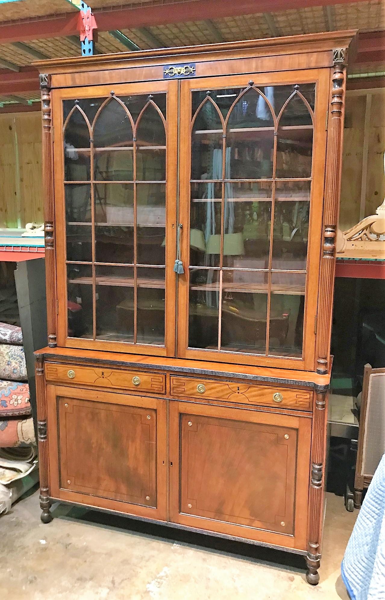 Outstanding 19th century English Sheraton bookcase or cabinet having a unique lion's head and harp accented cornice atop two glazed doors with arched astragal moldings. The lower section fitted with two drawers and cupboards featuring flame mahogany