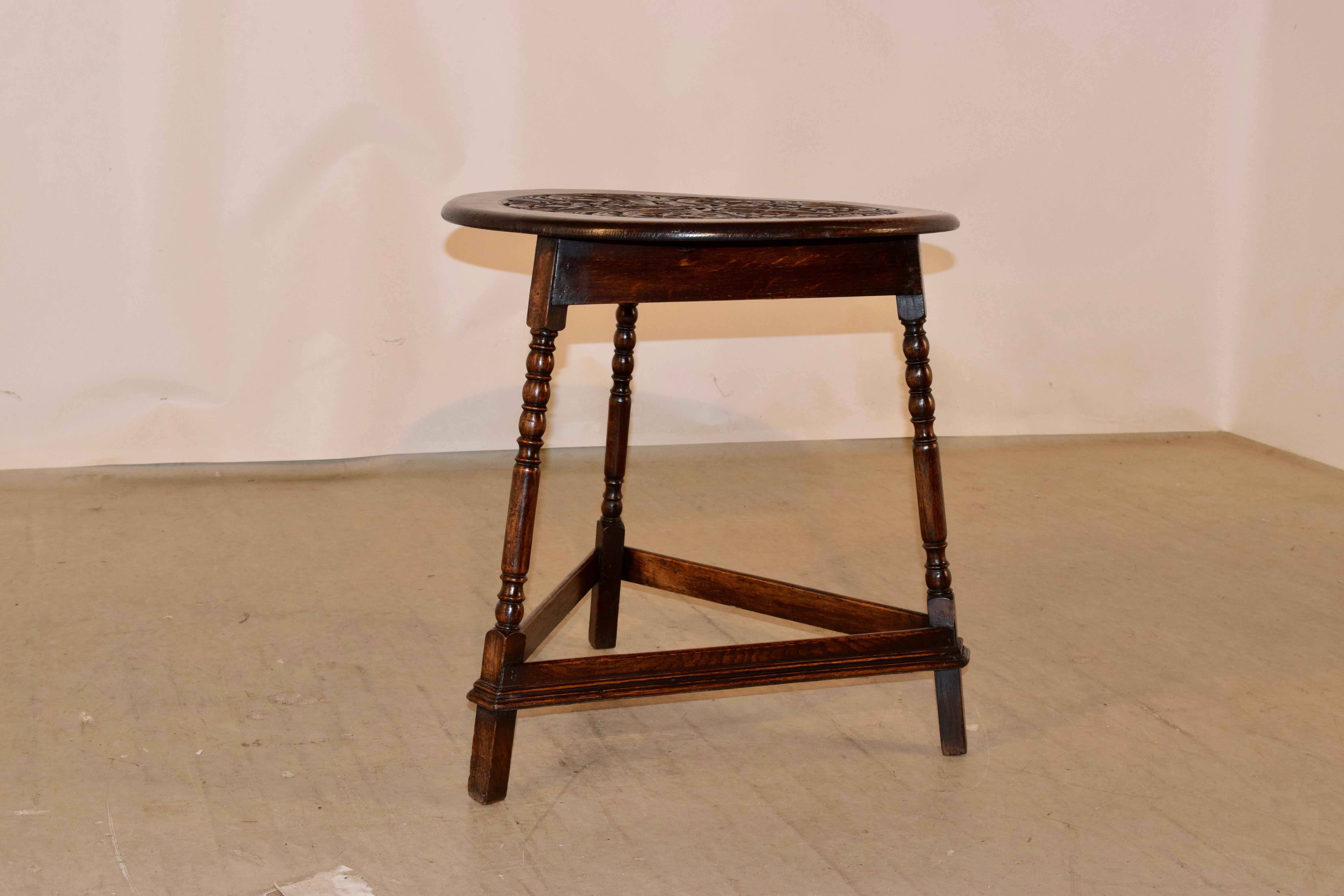 19th century oak side table from England with a fantastic hand carved decorated central medallion, surrounded by a banded edge, over a simple apron and supported on three hand turned legs, joined by molded stretchers.