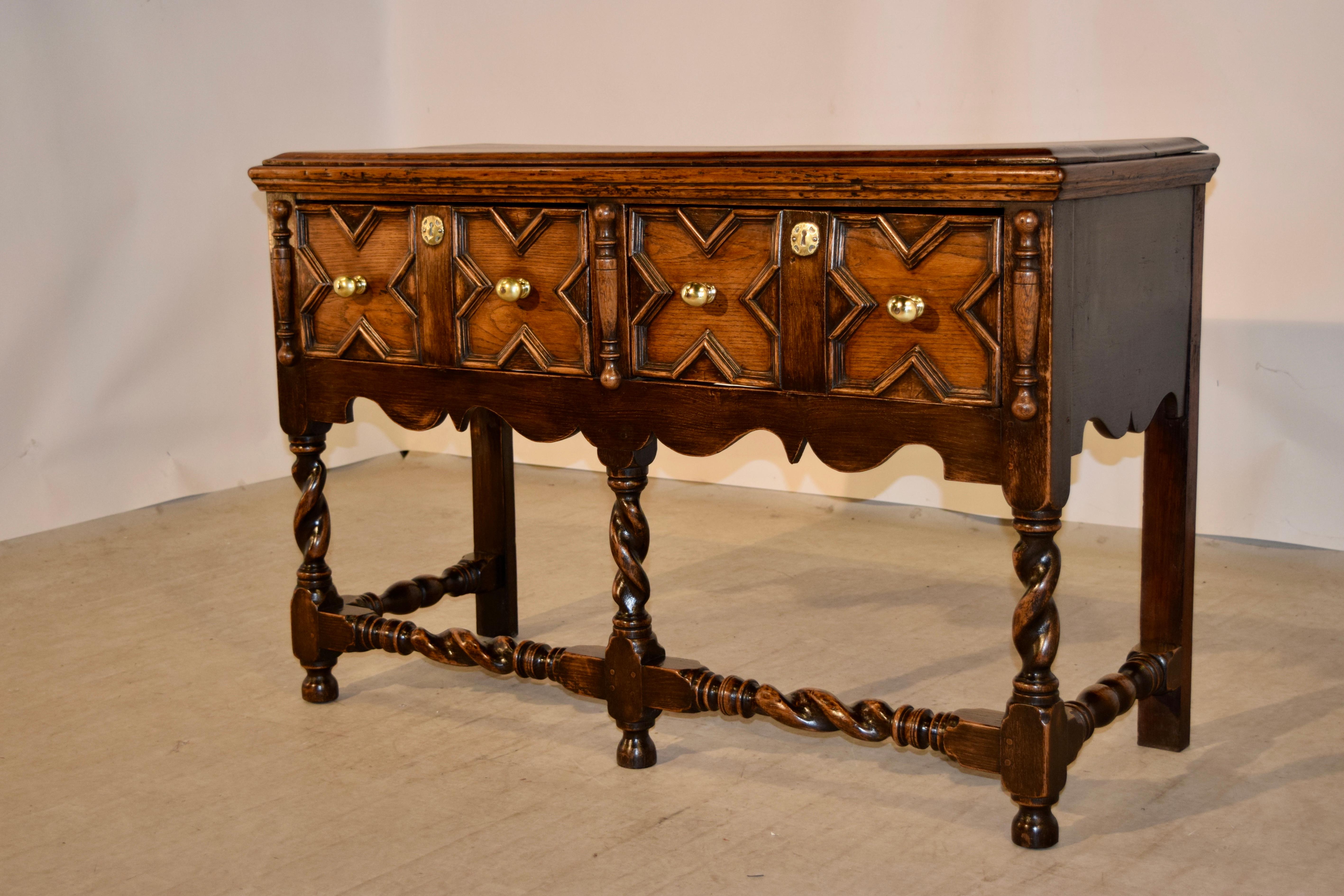 19th century English oak sideboard with a beveled edge around the top following down to simple sides with lovely scalloping on the aprons and two drawers in the front which are geometric raised paneled and are flanked by applied turnings. The piece