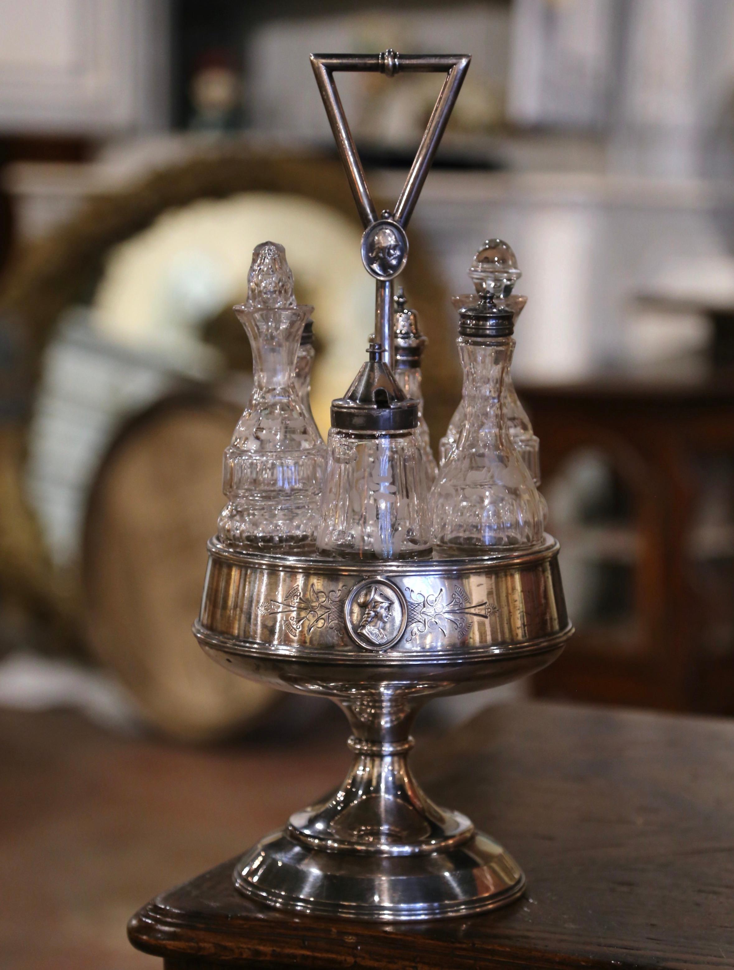 This cruet set was created in England circa 1880. Built of silver, the holder stands on a conforming circular base over a band decorated with repousse medallions of female figures. The display piece features six crystal containers, with includes a