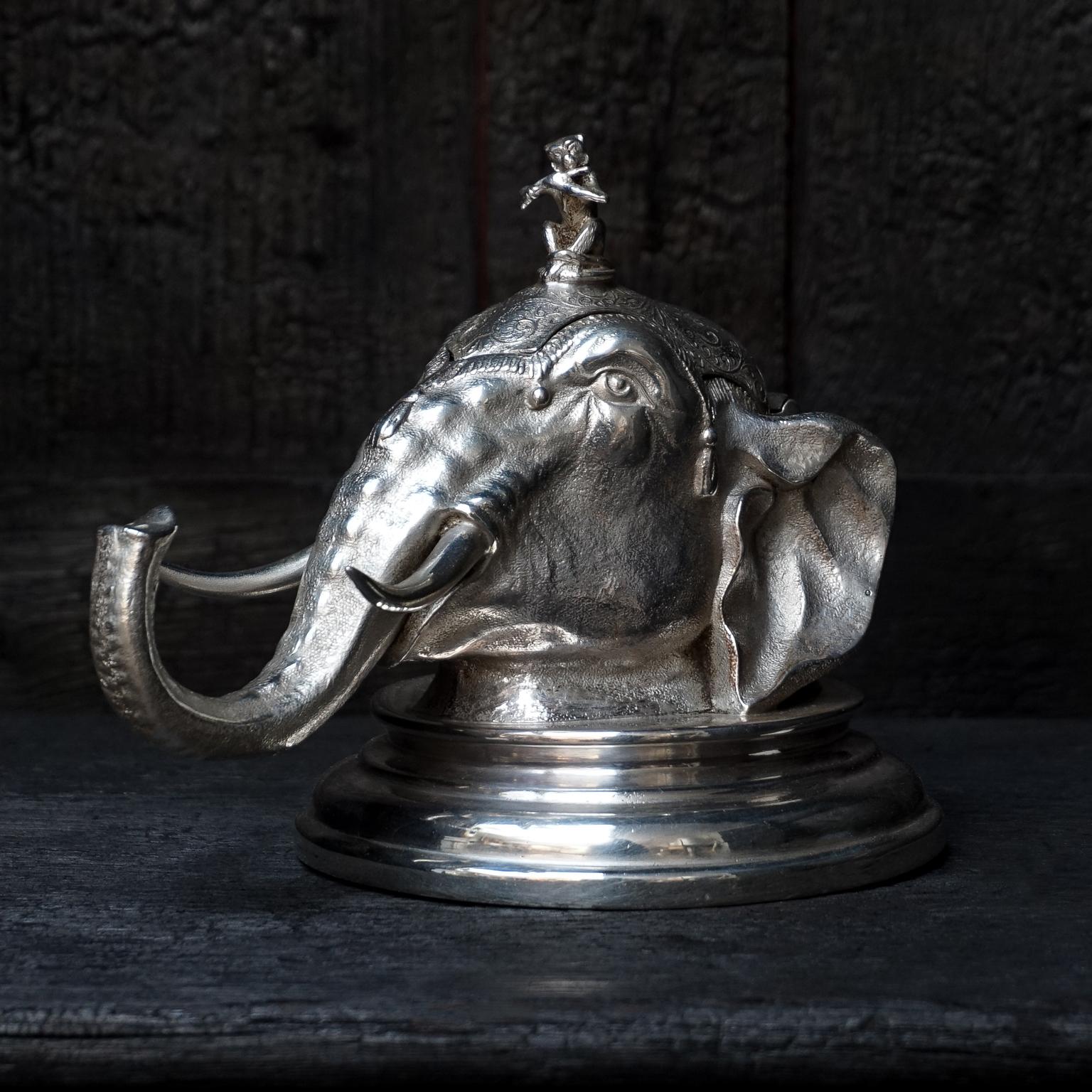 An exceptional English Victorian silver plate elephant head inkwell of the last quarter of the 19th century. 
Modelled like an Indian Parade elephant head with a monkey playing the flute on top. 
The head is placed on a circular base. It has a